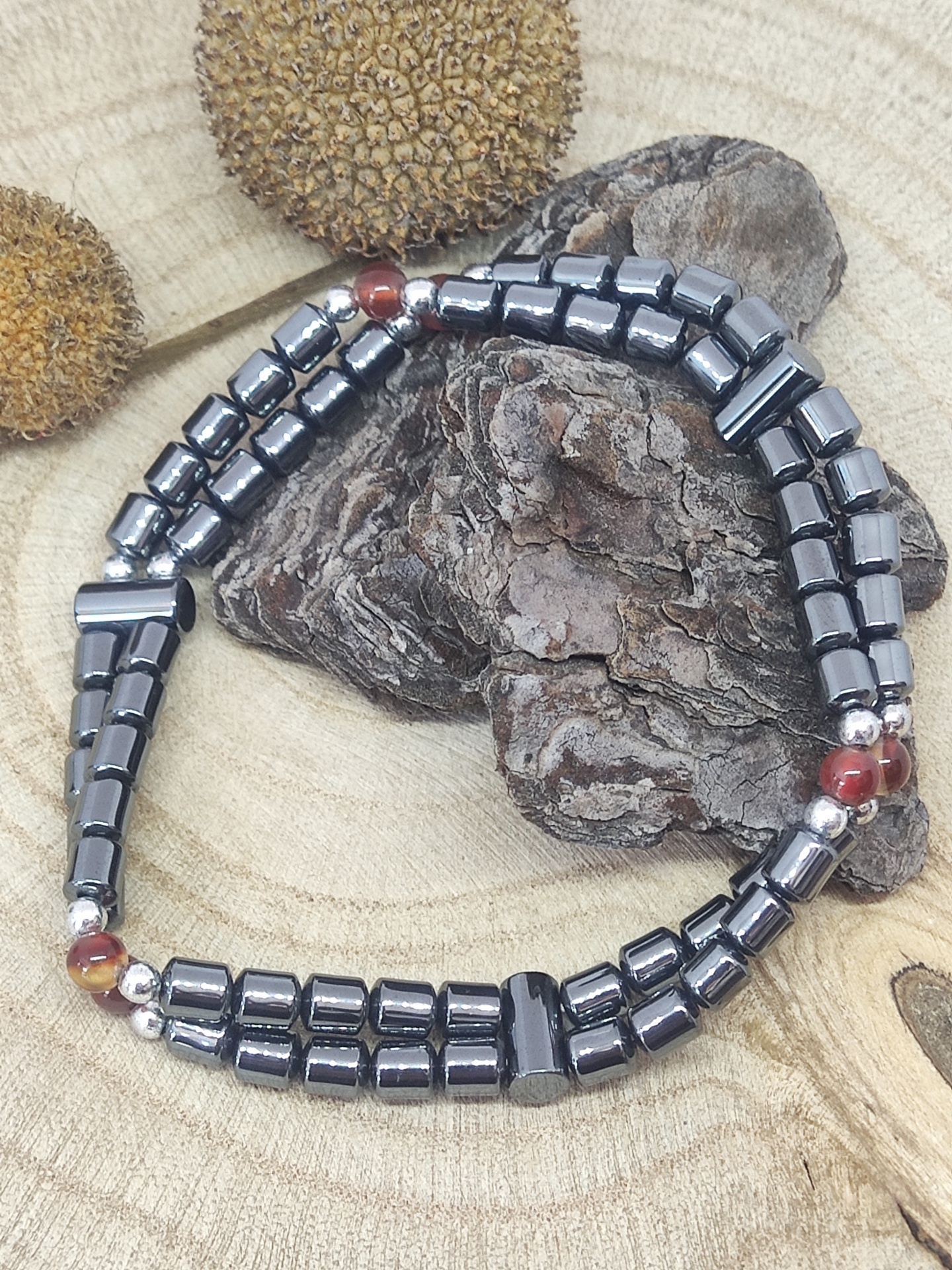 Pulseira preta e prateada com contas vermelhas sobre madeira e casca