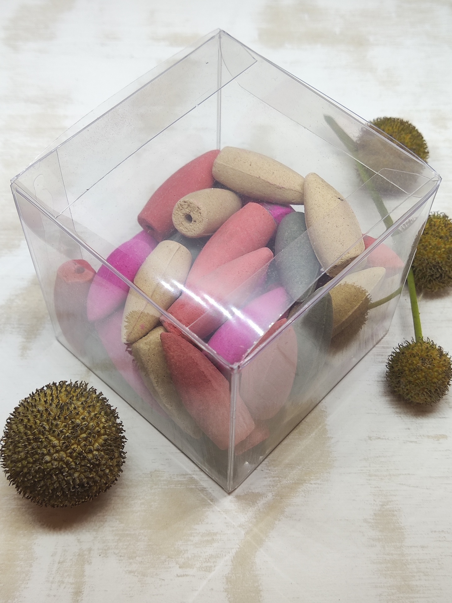 Caixa transparente cheia de contas de madeira coloridas ao lado de flores secas redondas