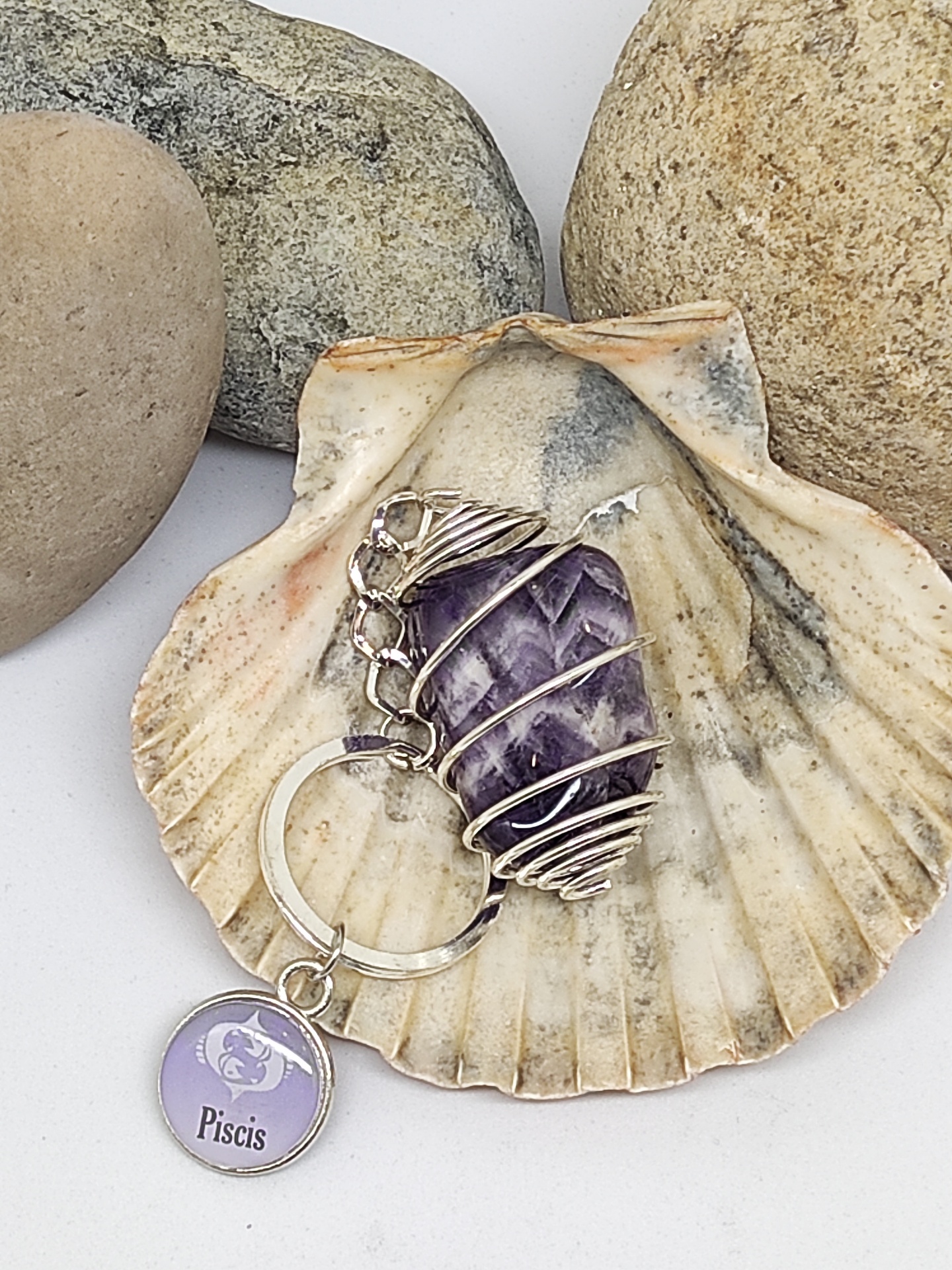 Chaveiro de pedra roxa e pendente PISCIS numa concha com pedras ao fundo