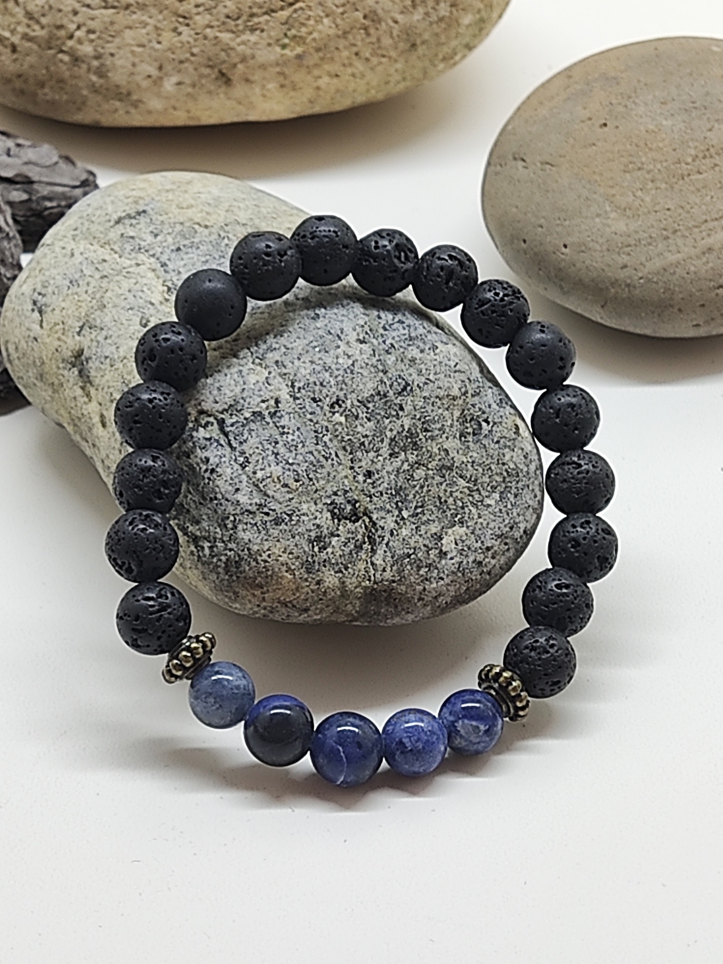 Pulseira de contas negras de lava vulcânica e azuis sobre pedras naturais