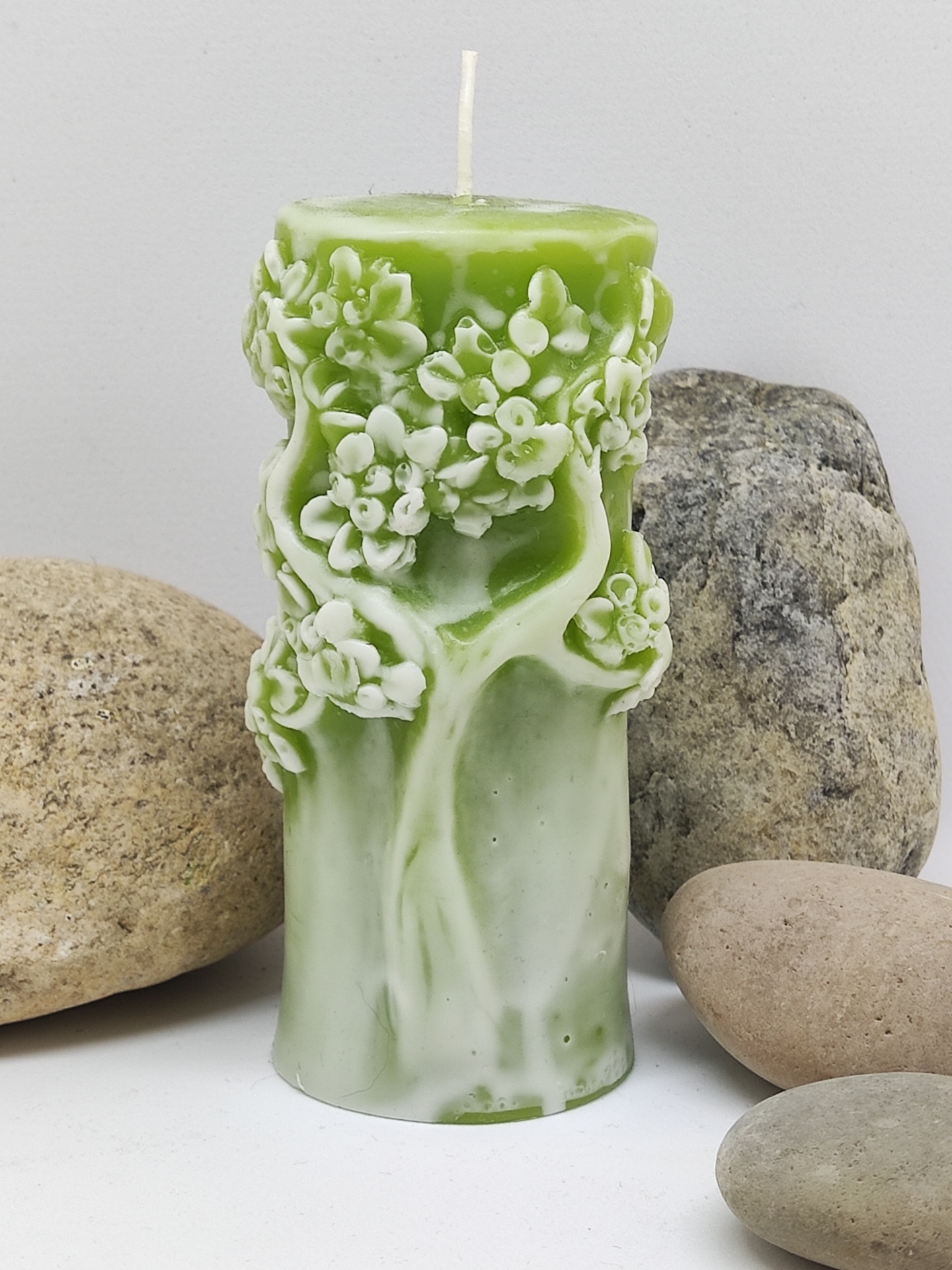 Vela verde decorativa com relevo de árvore e flores entre pedras