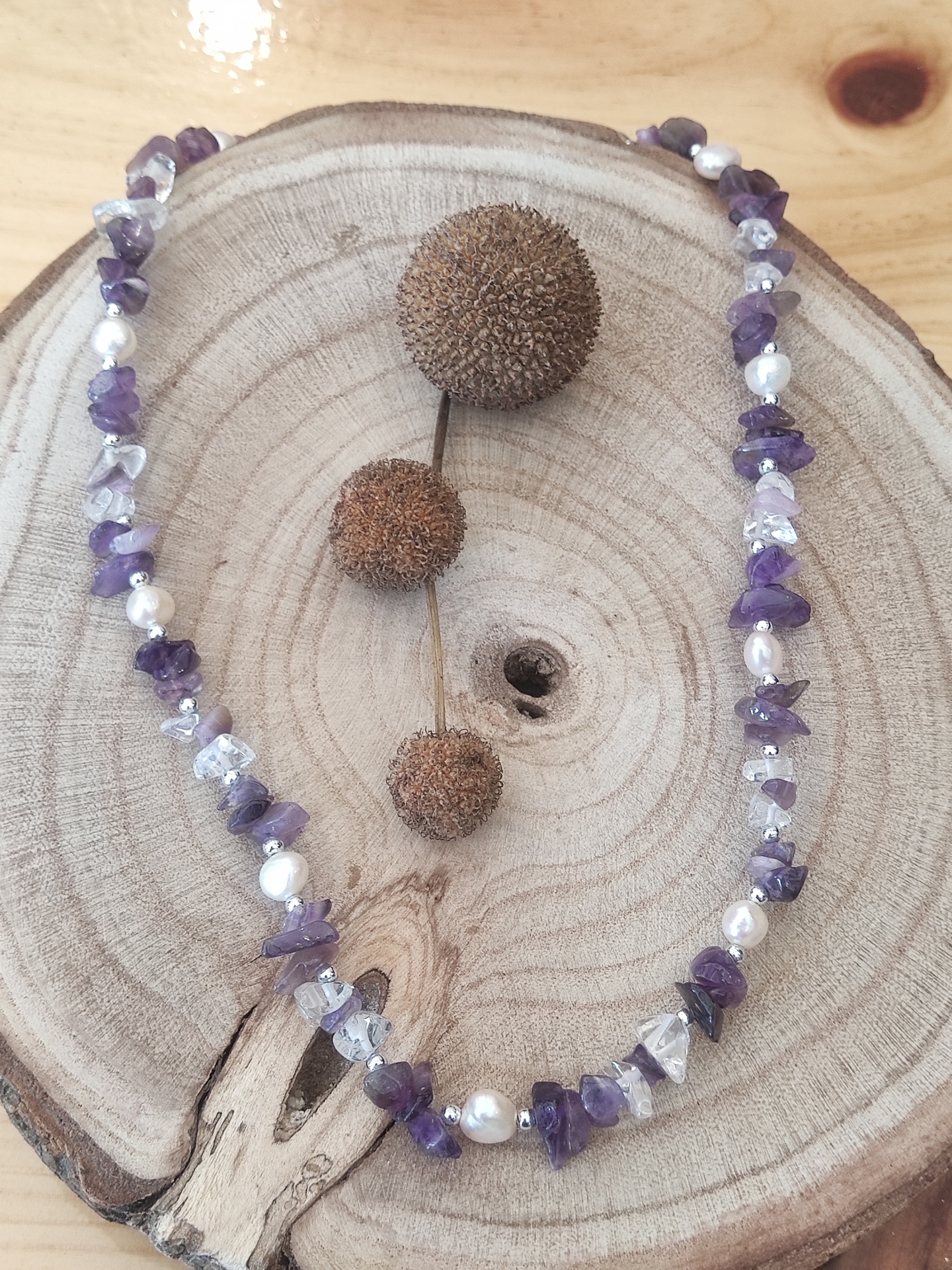 Colar de pedras roxas, transparentes e pérolas branca sobre base de madeira