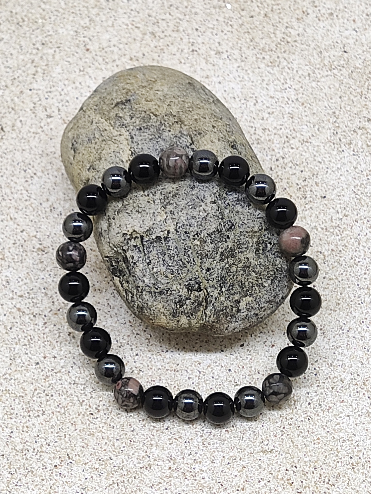 Pulseira de contas em preto, cinzento e castanho sobre pedra em areia