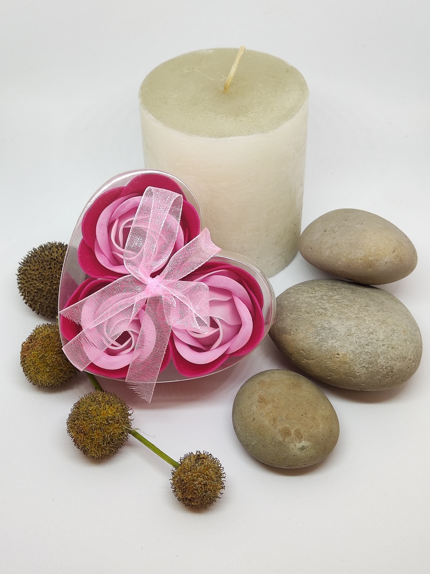 Conjunto decorativo com vela branca, pedras cinzentas, flores artificiais rosas em caixa coração com laço rosa e flores secas marrons
