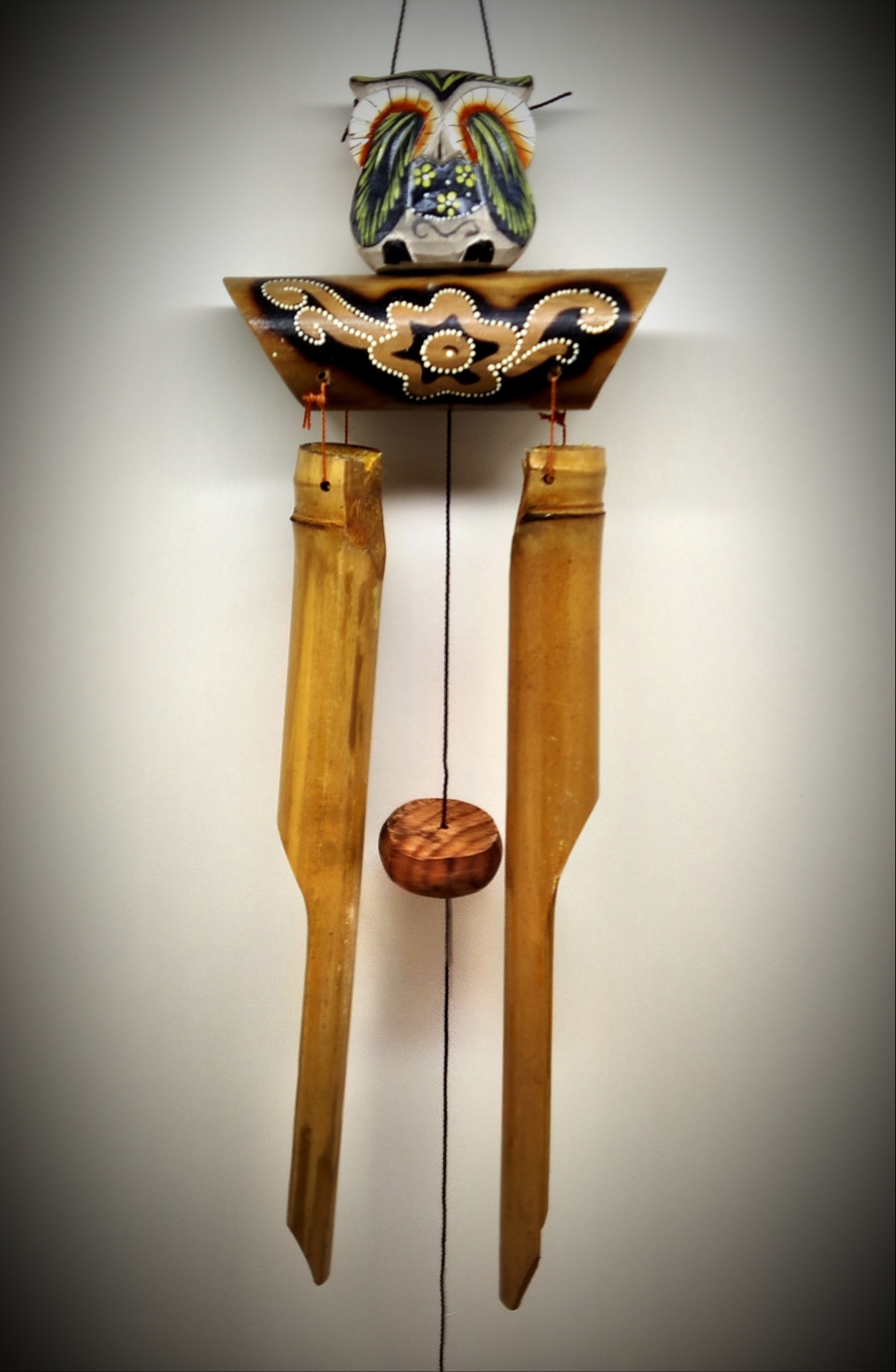 Objeto decorativo de madeira pendurado com coruja pintada e tubos de madeira longa
