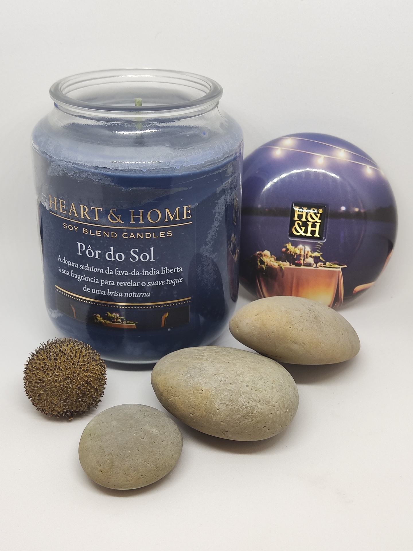 Vela em frasco de vidro azul com tampa roxa, pedras e fruto seco