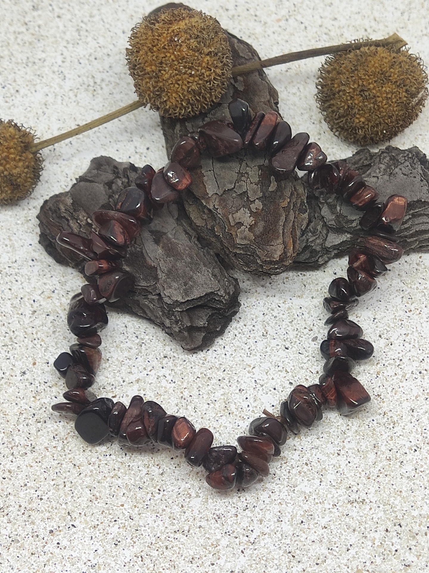 Pulseira de pedras castanho-avermelhadas sobre casca de árvore e flores secas