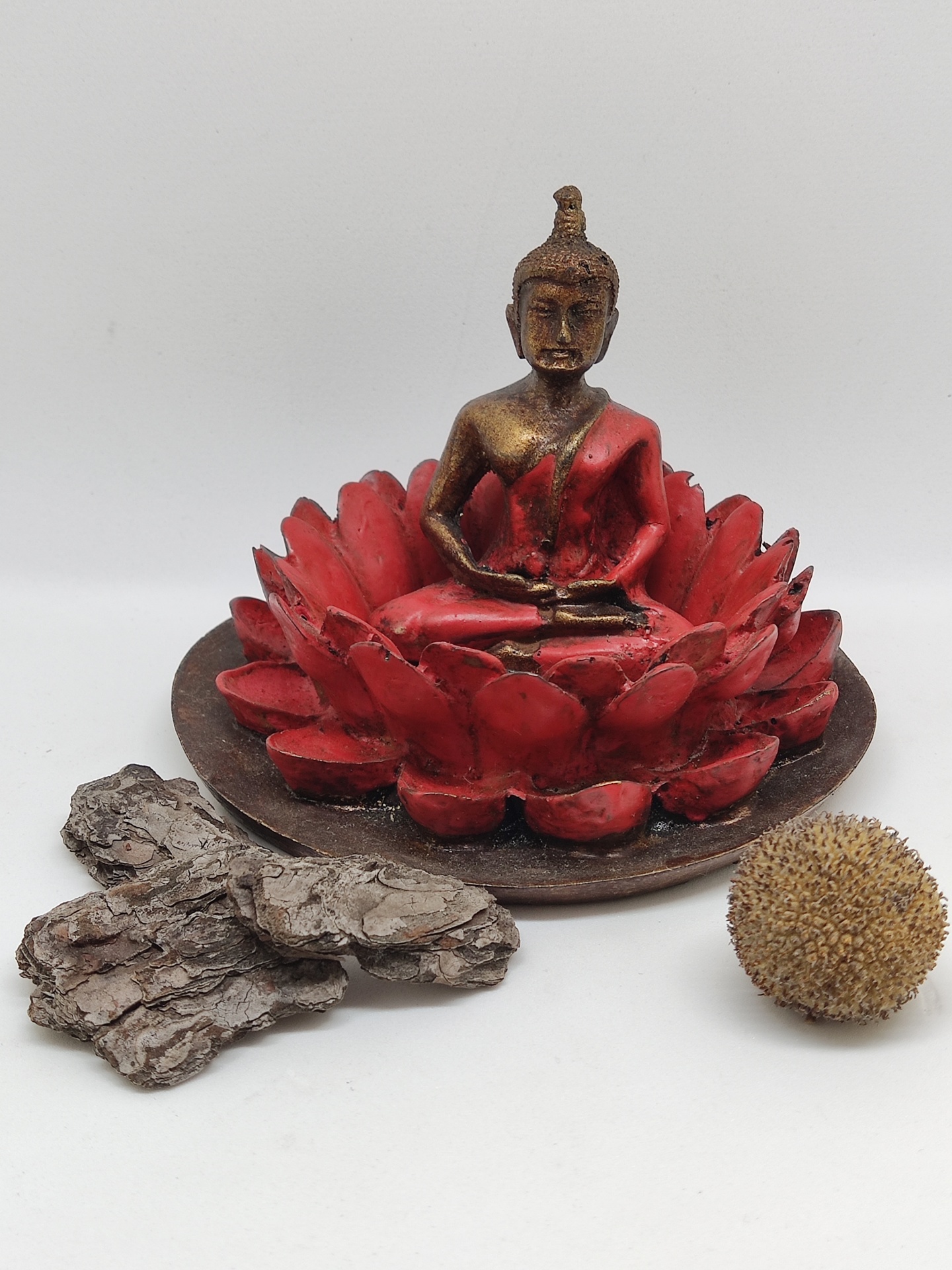 Estátua de Buda dourada com roupa vermelha numa base de lótus vermelha com cascas de árvore e bola texturizada