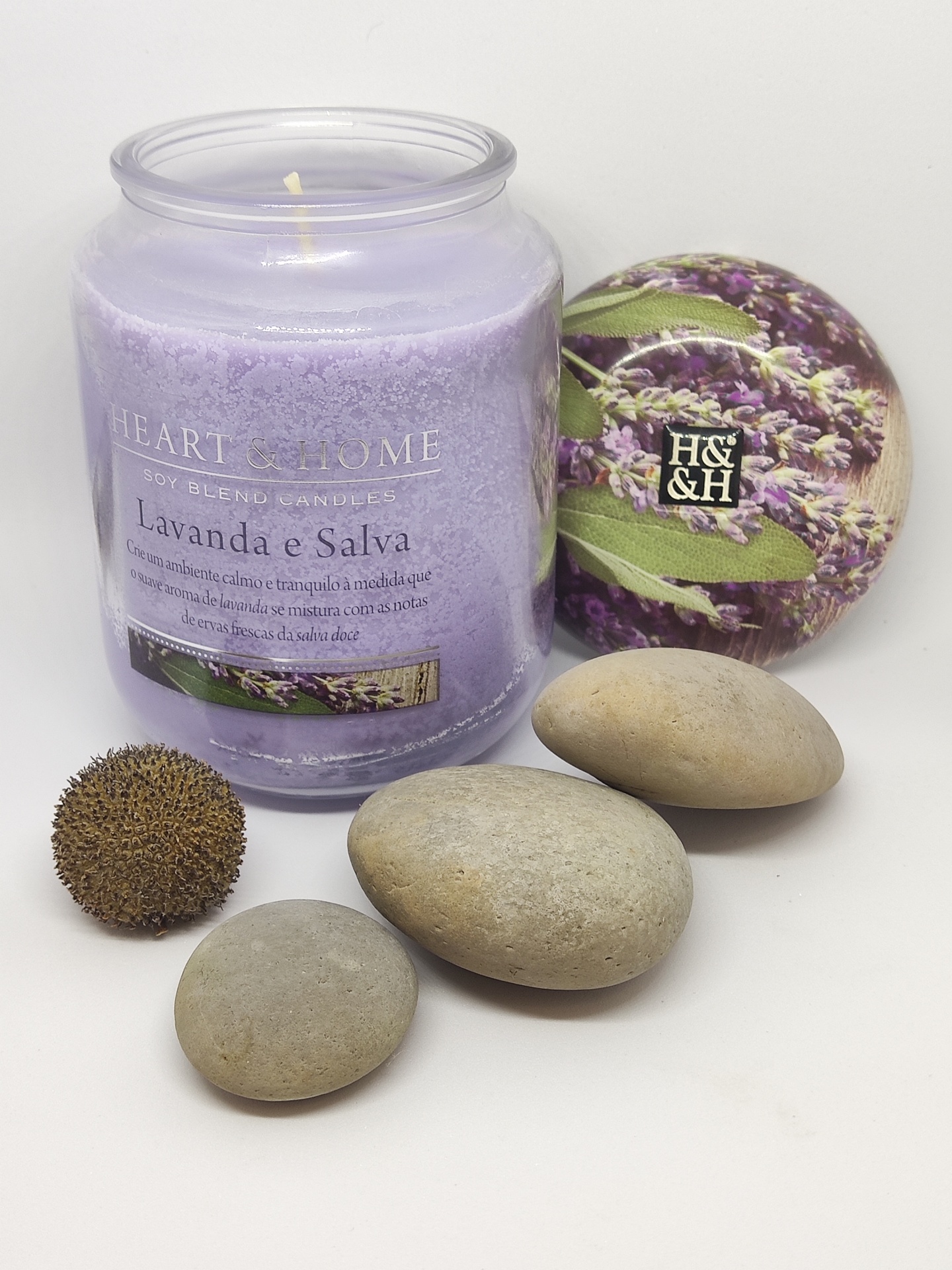 Vela lilás em vidro com tampa de lavanda, pedras cinzentas e planta seca