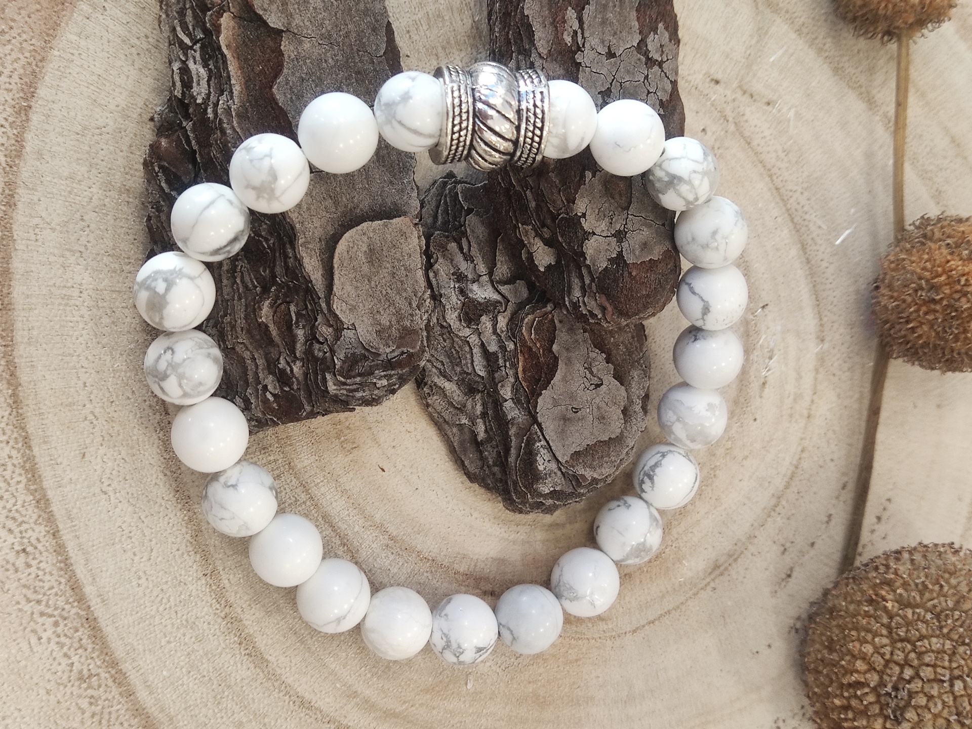 Pulseira de contas brancas com veios cinzentos e contas metálicas prateadas numa base de madeira