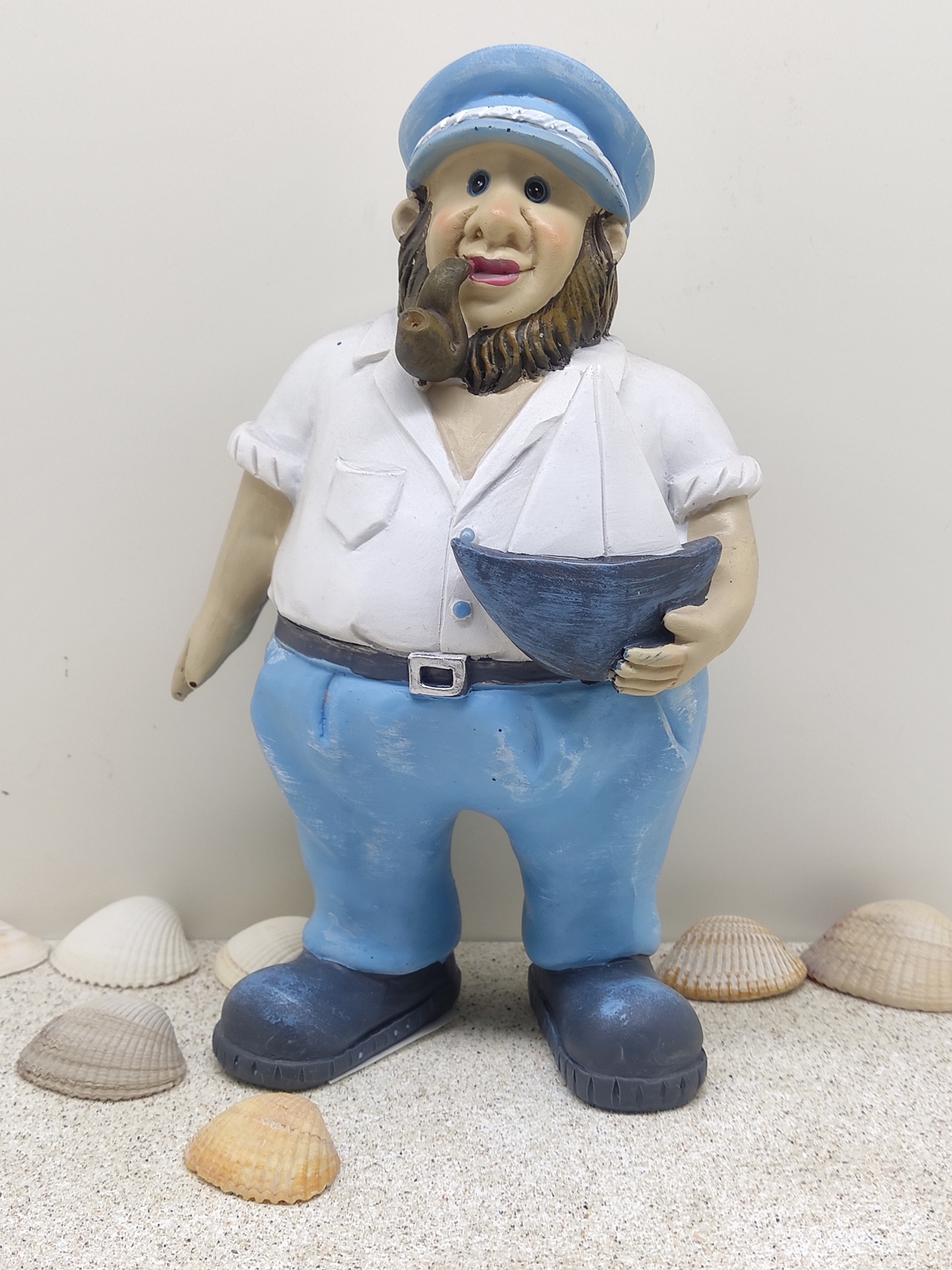 Estátua de marinheiro com barco e conchas sobre areia
