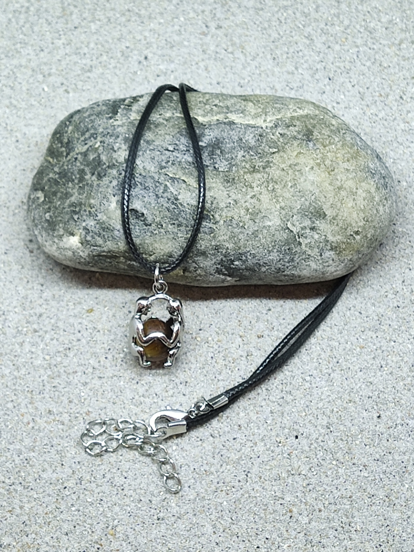 Colar com pendente de pedra castanha e fio preto sobre pedra cinzenta