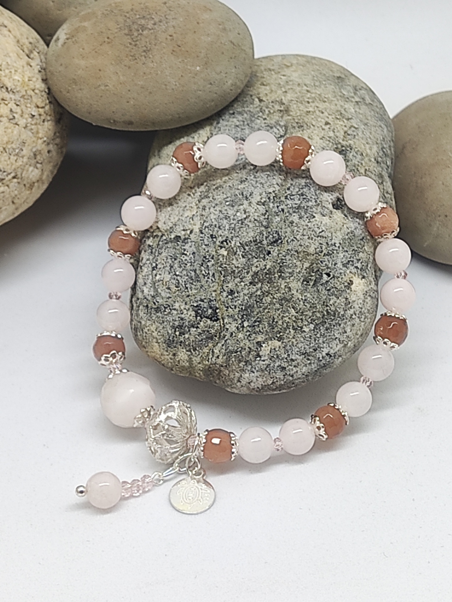 Pulseira com contas rosa e castanho sobre pedras naturais cinza e bege