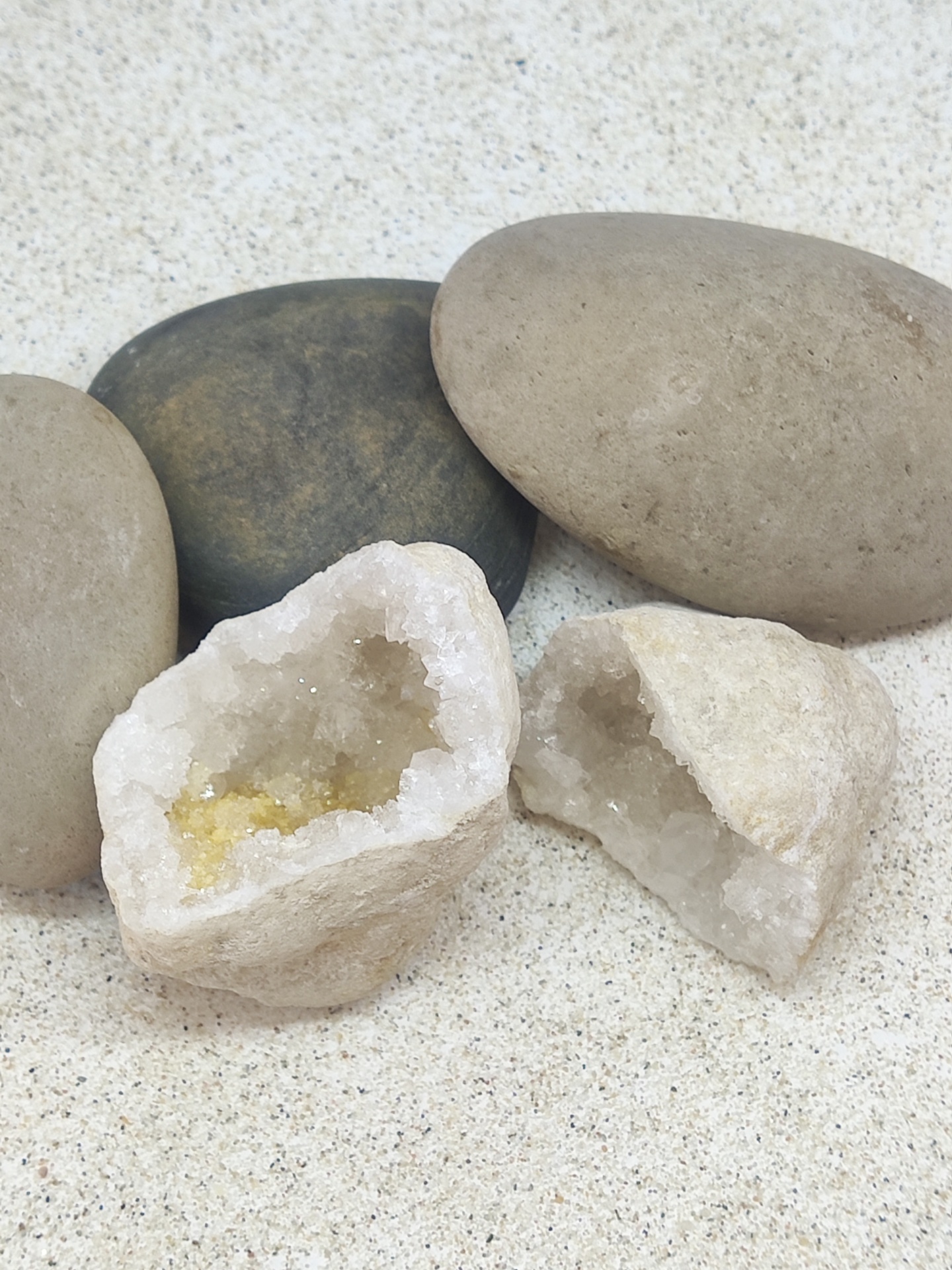 Pedras lisas cinza e geodas abertas com cristais em superfície clara