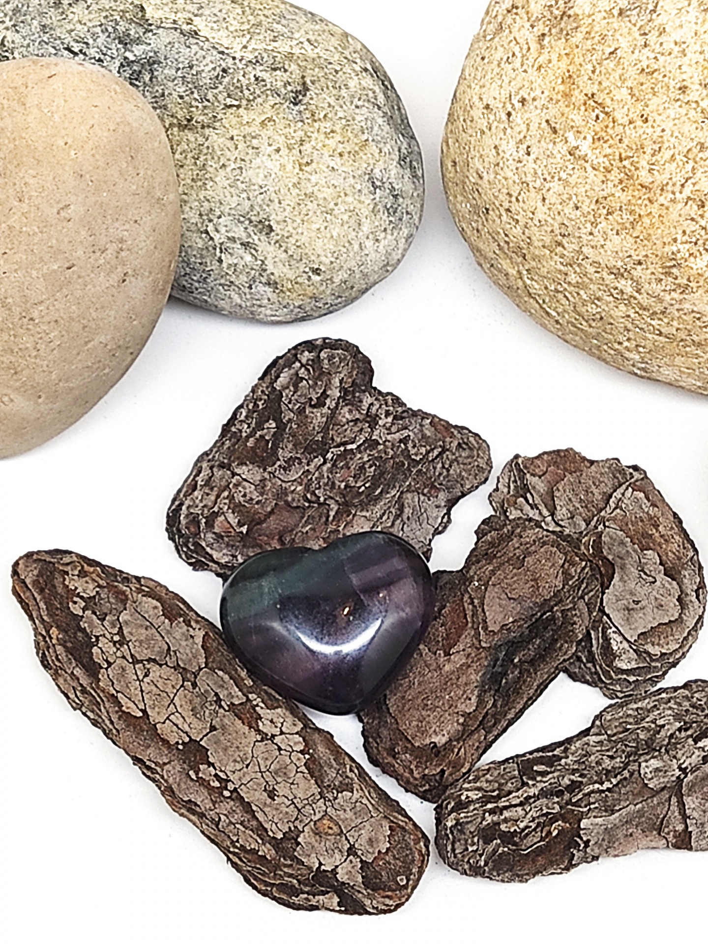 Coração de pedra polida azul e verde sobre cascas de árvore e pedras claras.