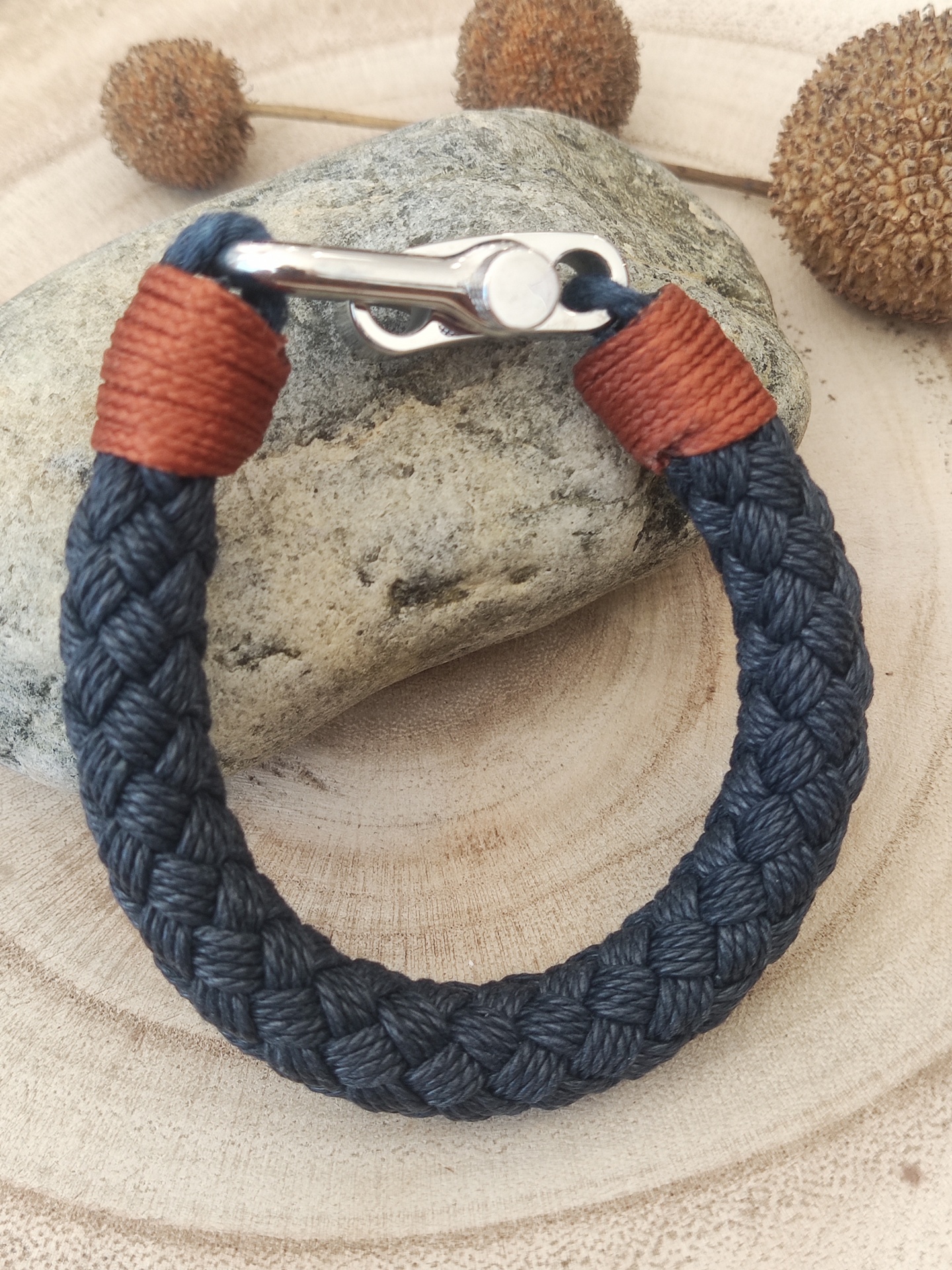 Pulseira trançada azul escura com fecho metálico sobre pedra e fundo de madeira