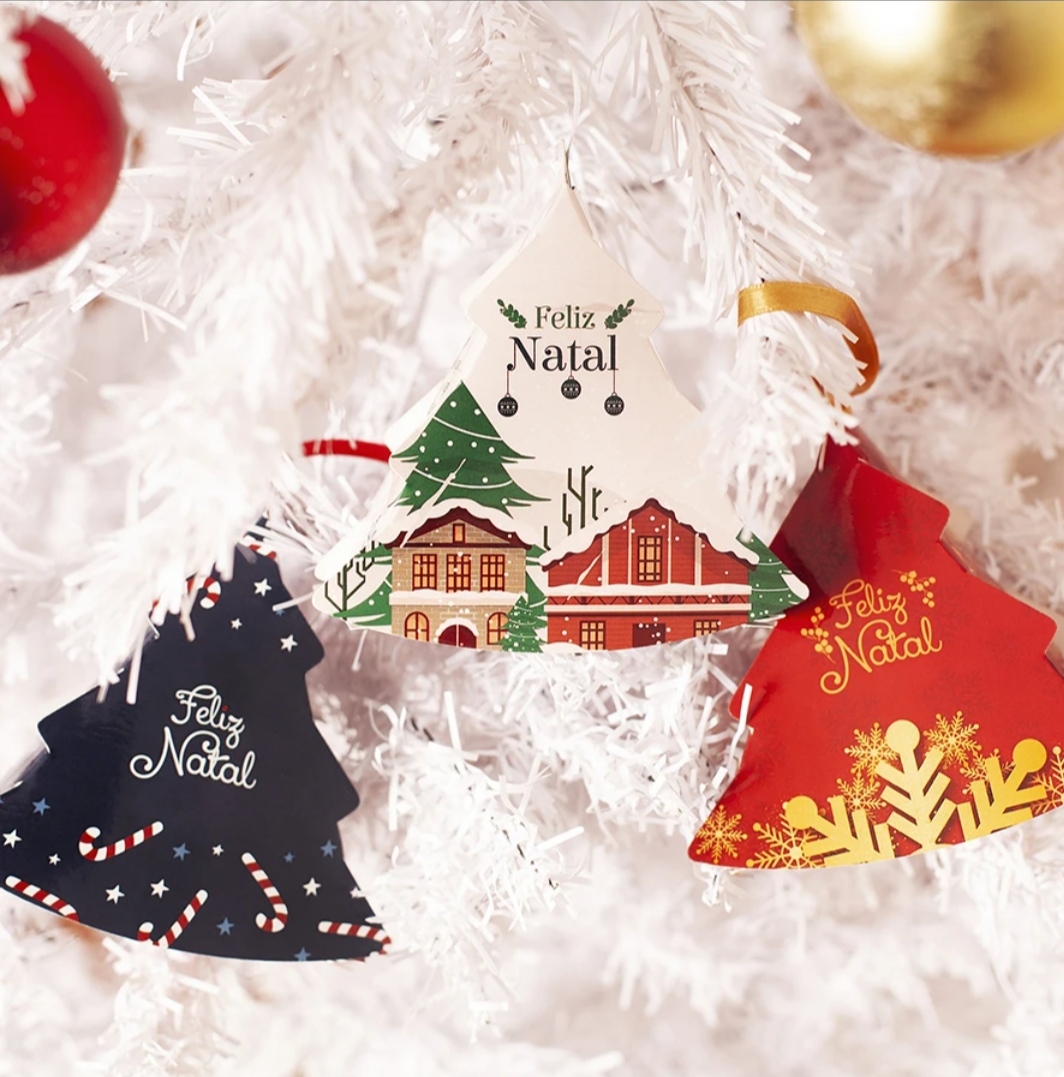 Pendentes decorativos de Natal em forma de árvore com mensagens e ilustrações, pendurados em árvore artificial branca.