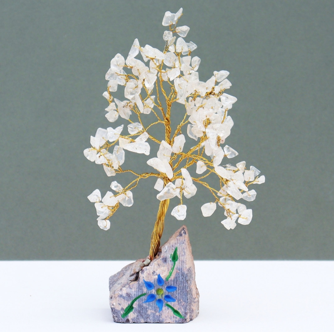 Árvore decorativa de fios dourados com pedras brancas numa base de pedra pintada com flor azul.