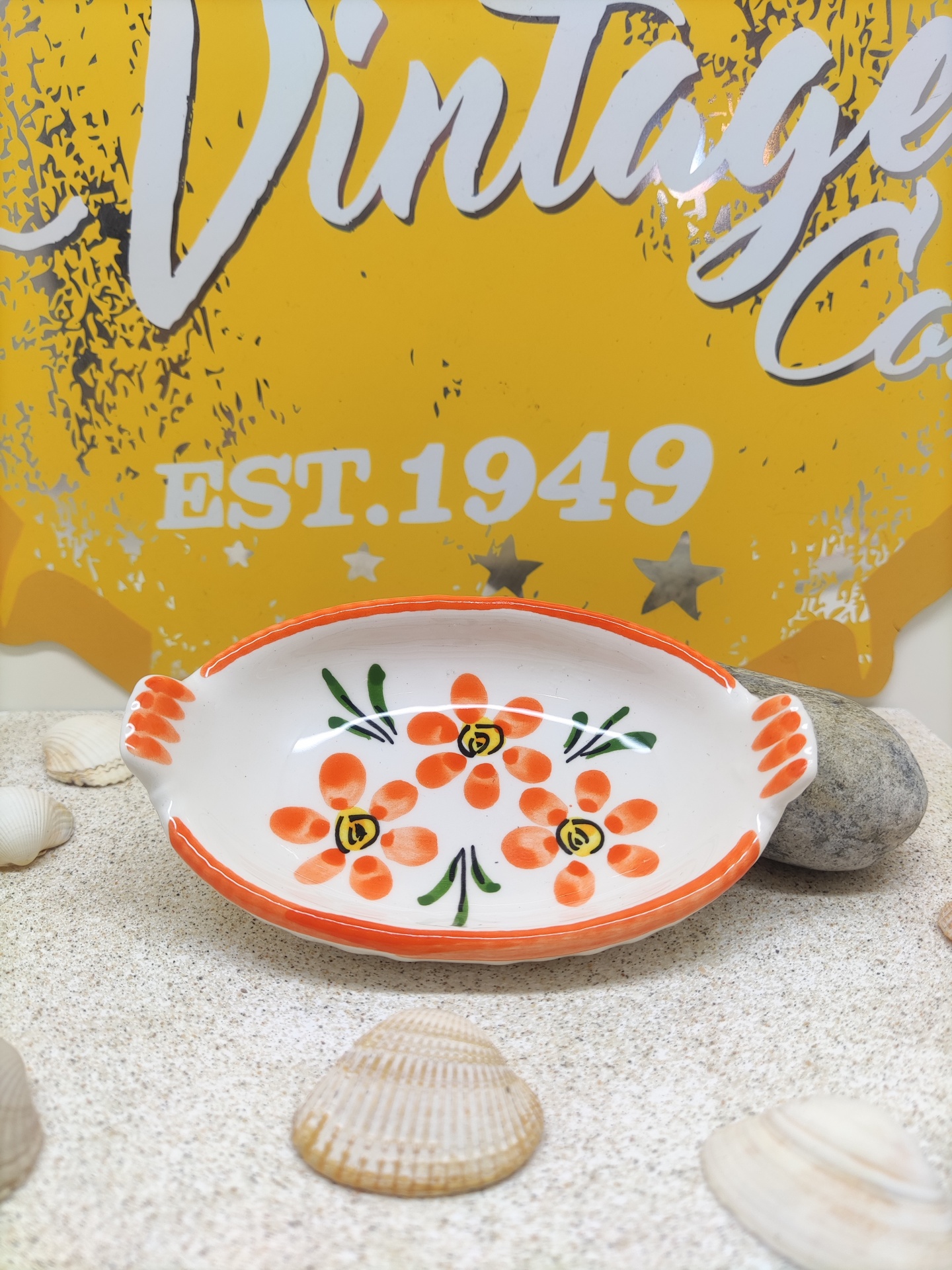 prato oval decorativo com flores laranja sobre mesa com conchas e fundo amarelo