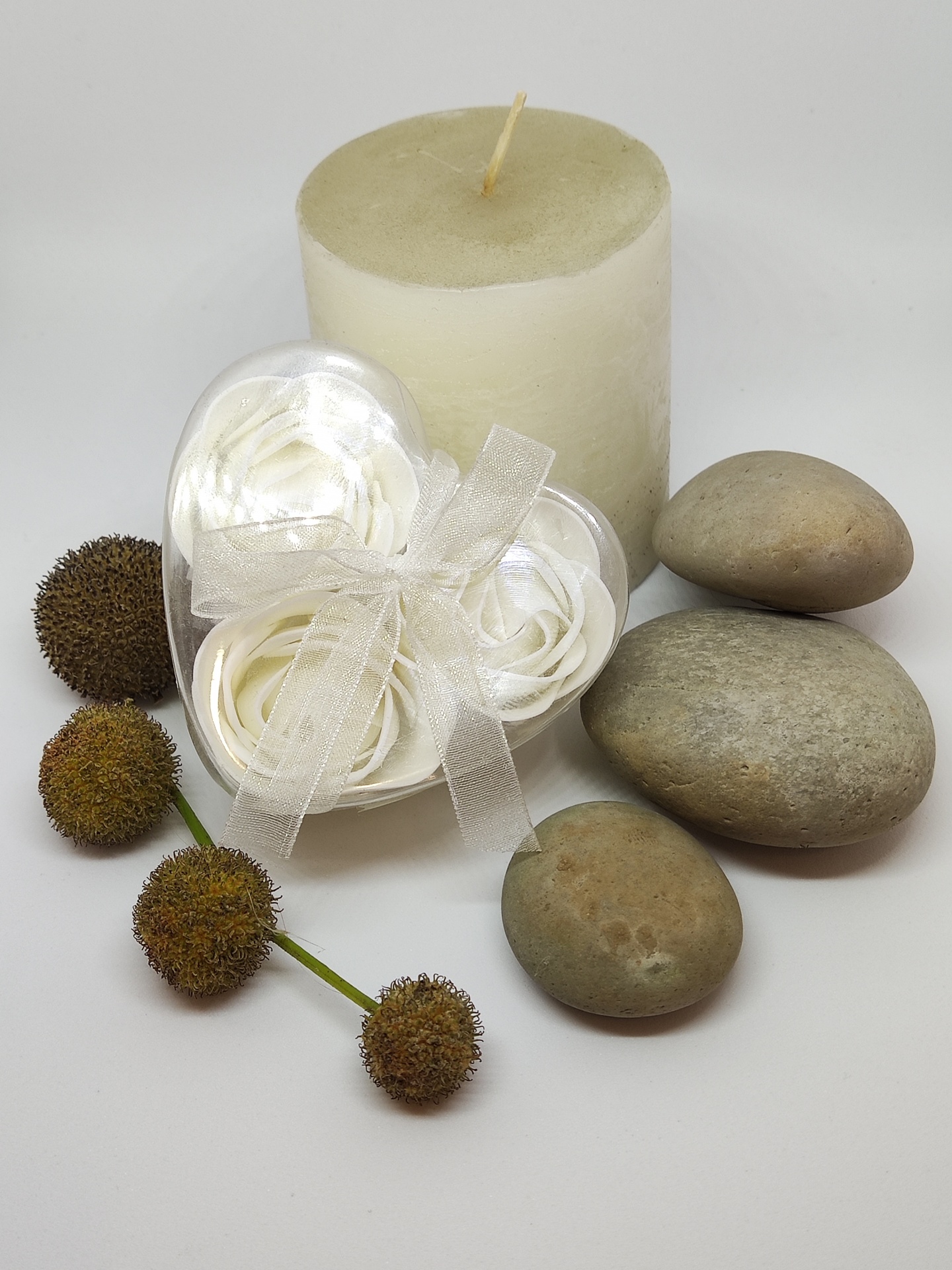 Conjunto decorativo com vela branca, pedras cinza, flores artificiais brancas e flores secas castanhas