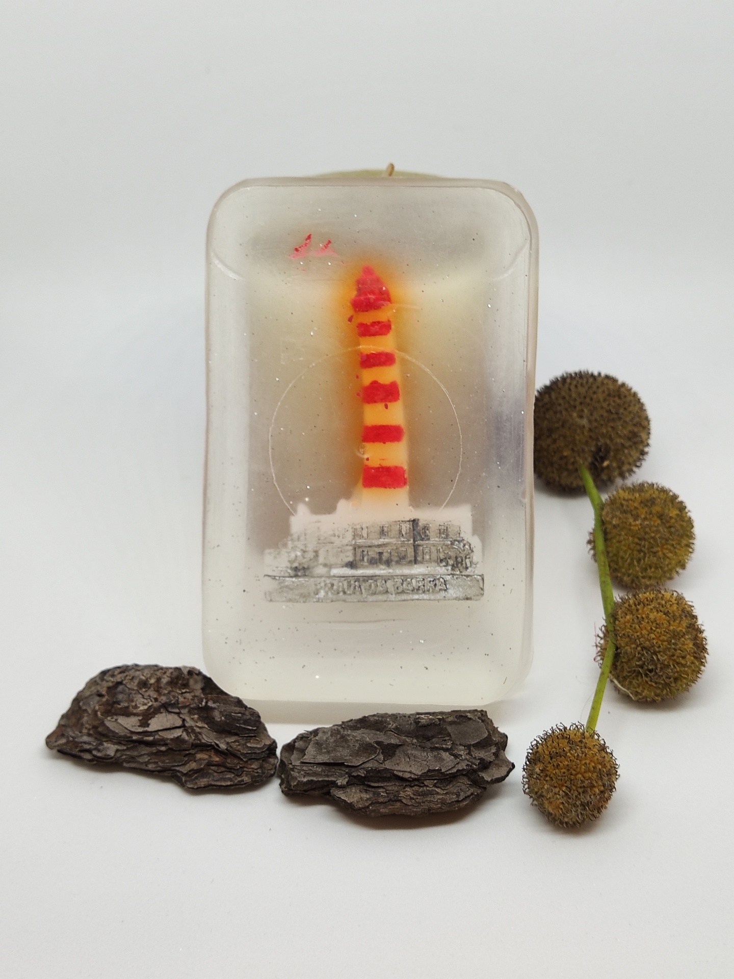 Vela com figura de farol e elementos naturais ao redor sobre fundo branco