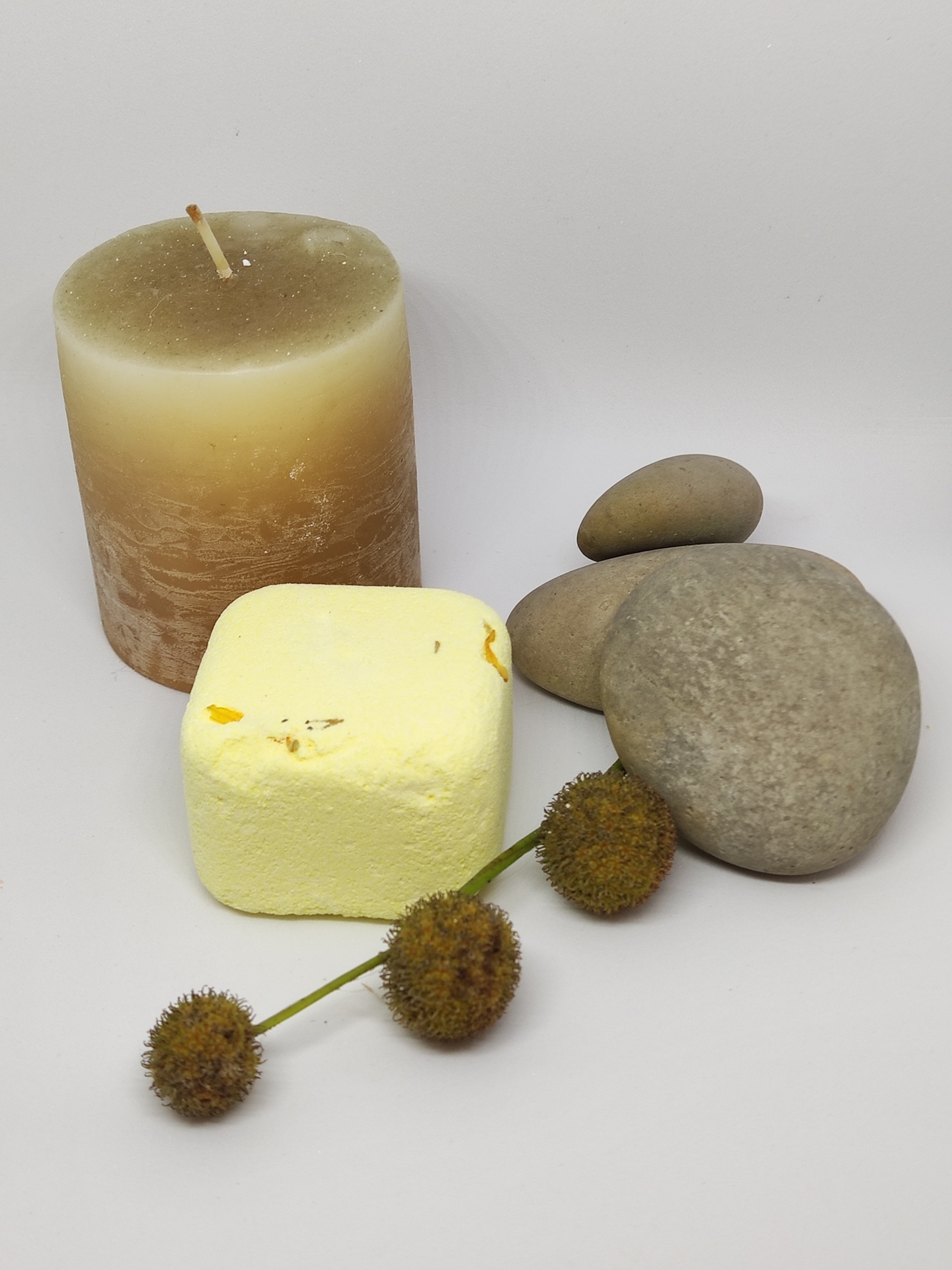 Vela bege, cubo amarelo, três pedras cinzentas e ramo com bolas secas marrons