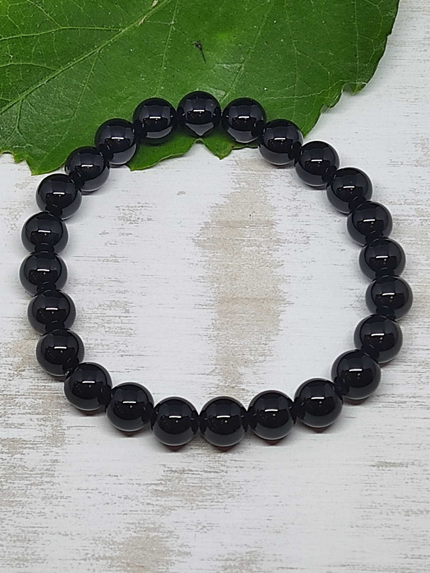 Pulseira de contas pretas brilhantes sobre superfície branca com folha verde