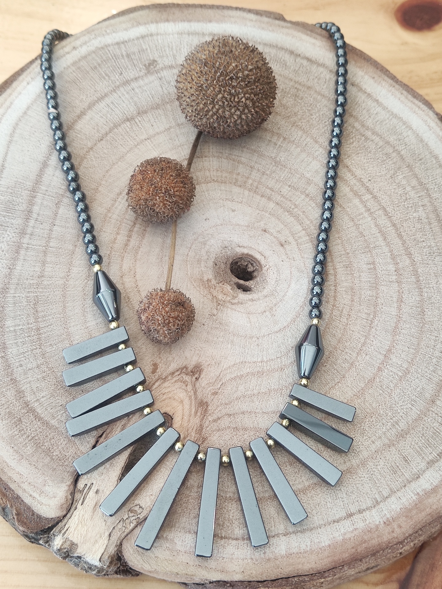 Colar com barras cinzentas e contas pretas sobre madeira com bolas secas