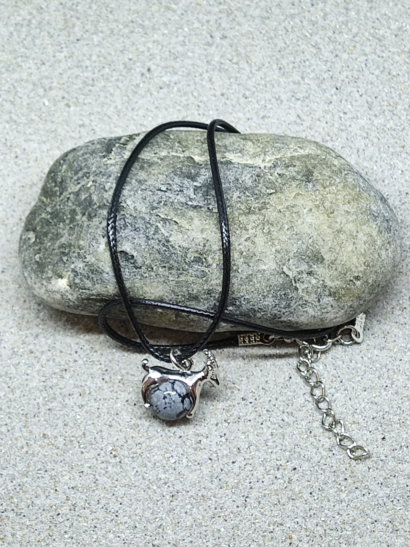 Colar com pendente em forma de camelo com pedra, cordão preto, sobre pedra e areia.