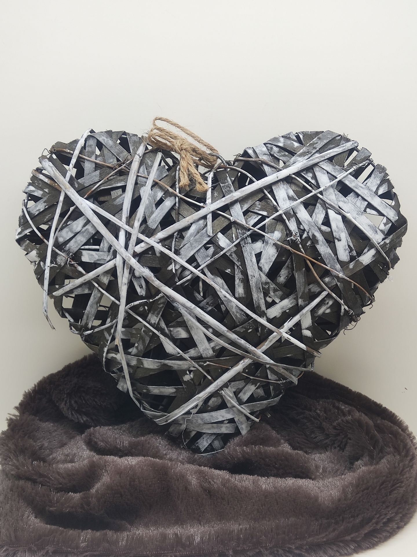 Coração metálico decorativo prateado entrelaçado em arame, apoiado em tecido castanho peludo