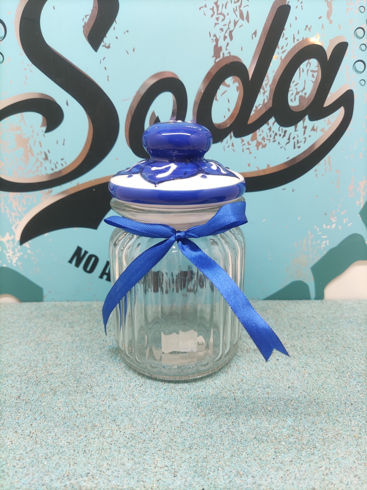 Frasco de vidro com tampa cerâmica e fita azul diante de fundo com texto