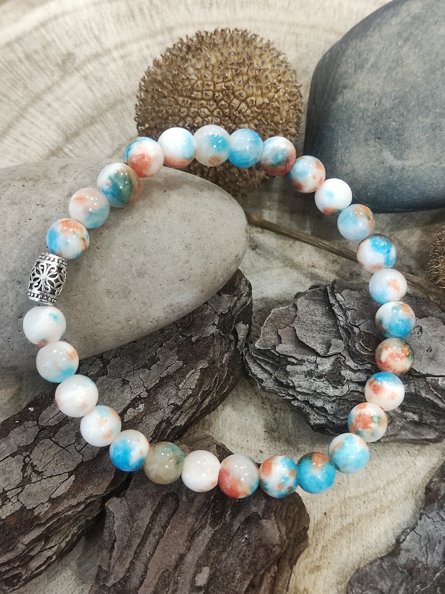 Pulseira de contas coloridas em pedra com detalhe metálico prateado sobre elementos naturais