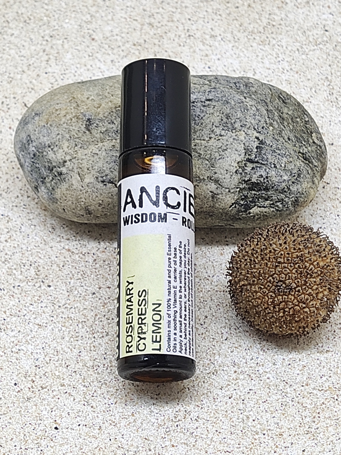 Frasco pequeno de roll-on com etiqueta branca e amarela ao lado de pedra e semente sobre superfície clara