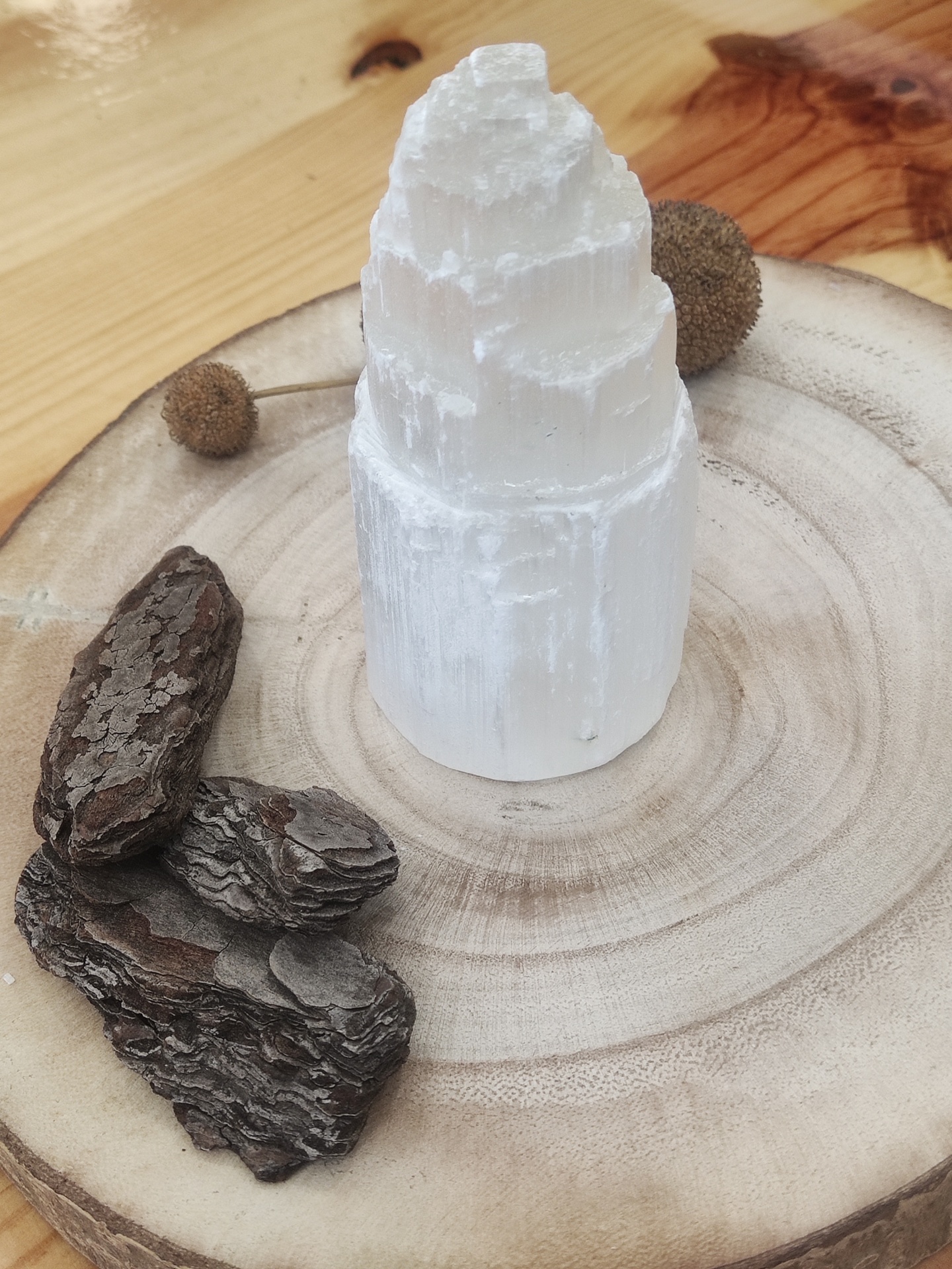 Escultura branca em forma de torre sobre base de madeira com casca de árvore e sementes à volta