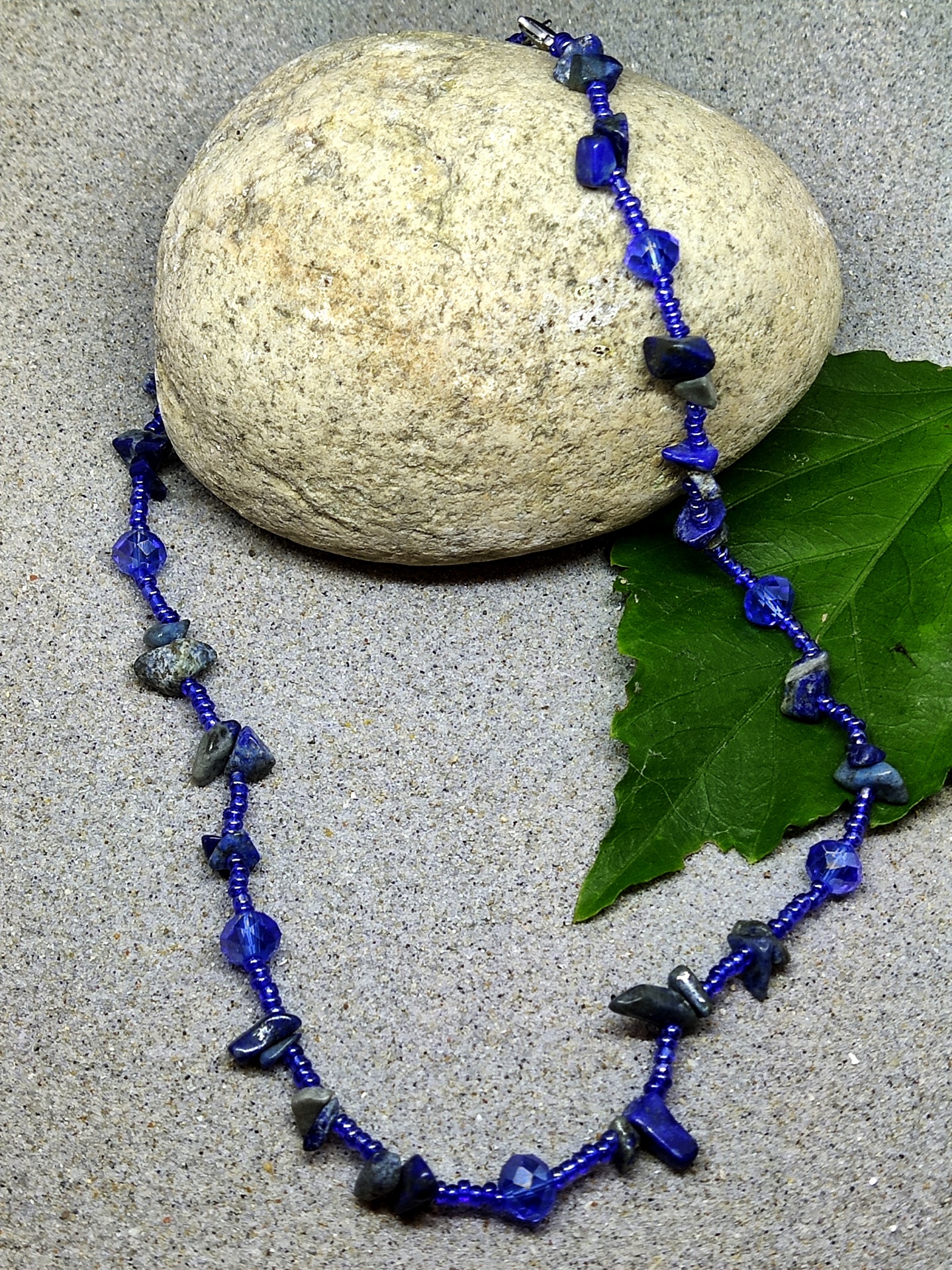 Colar azul com pedras escuras sobre pedra clara e folha verde