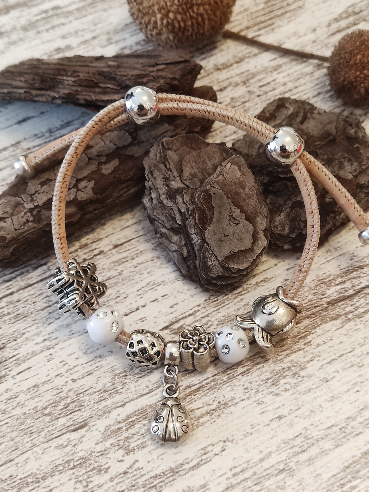 Pulseira com contas e pendentes prateados e brancos sobre madeira clara