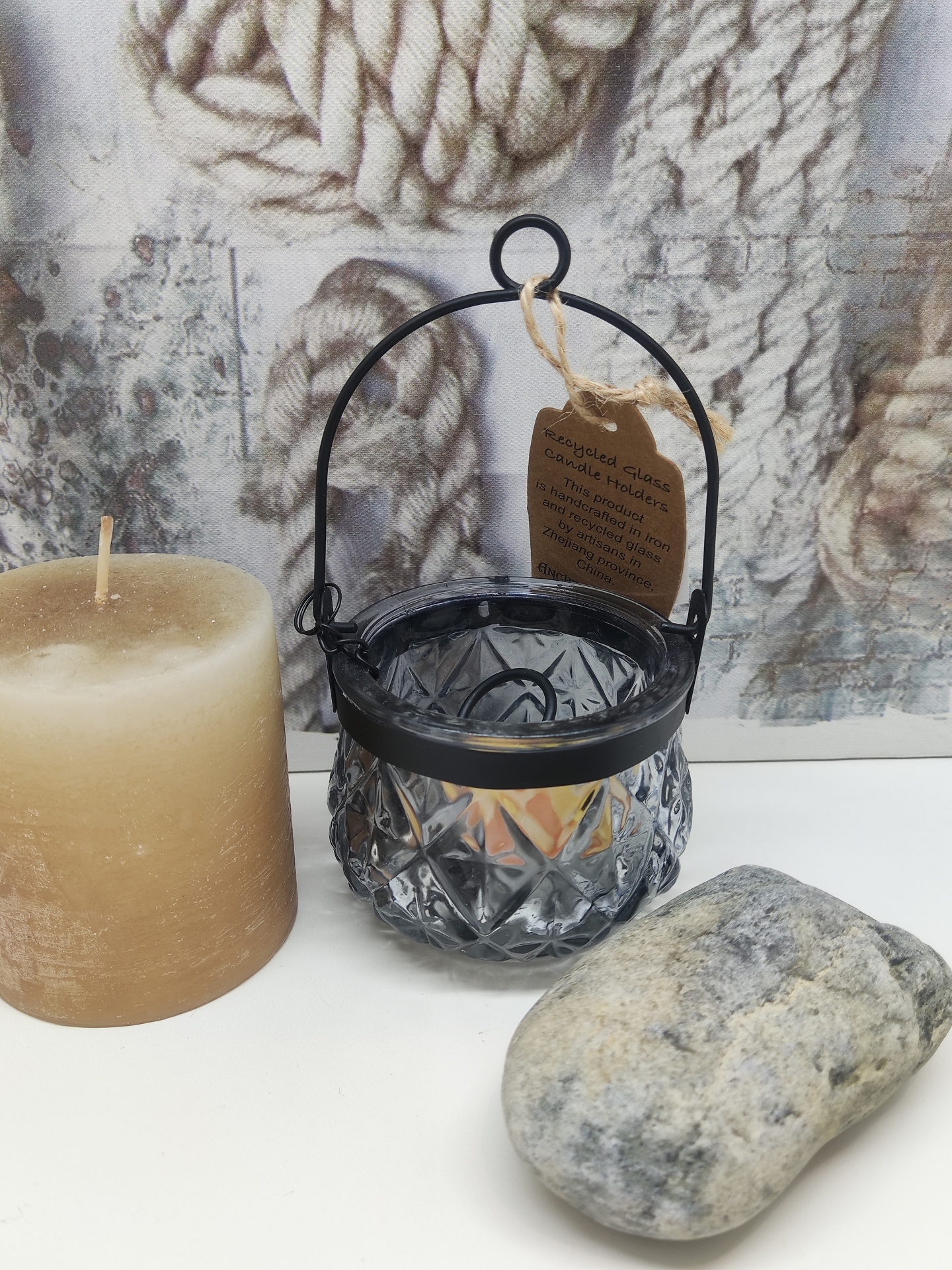 Vela castanha, lanterna de vidro cinzento com suporte preto, pedra cinzenta em mesa branca