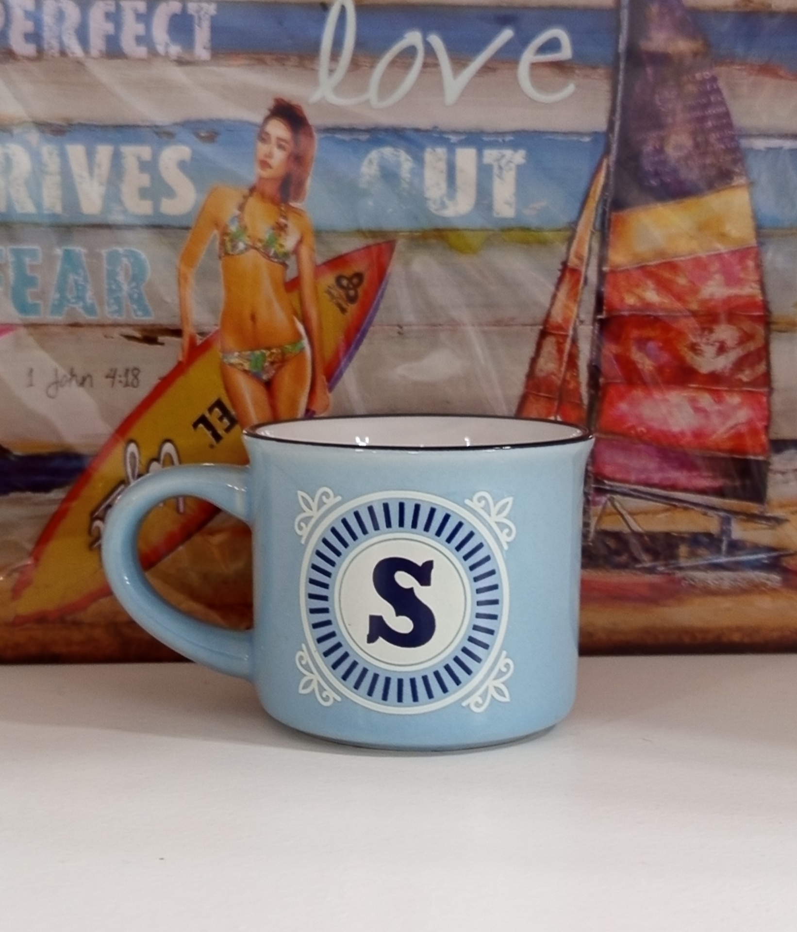 Caneca azul clara com letra S em fundo decorativo azul e branco