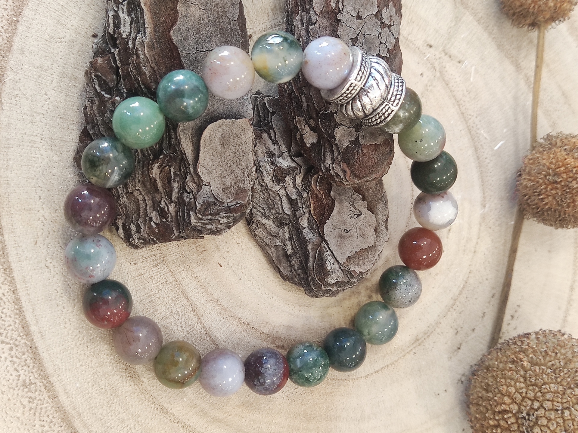 Pulseira colorida com conta metálica sobre base de madeira e casca de árvore