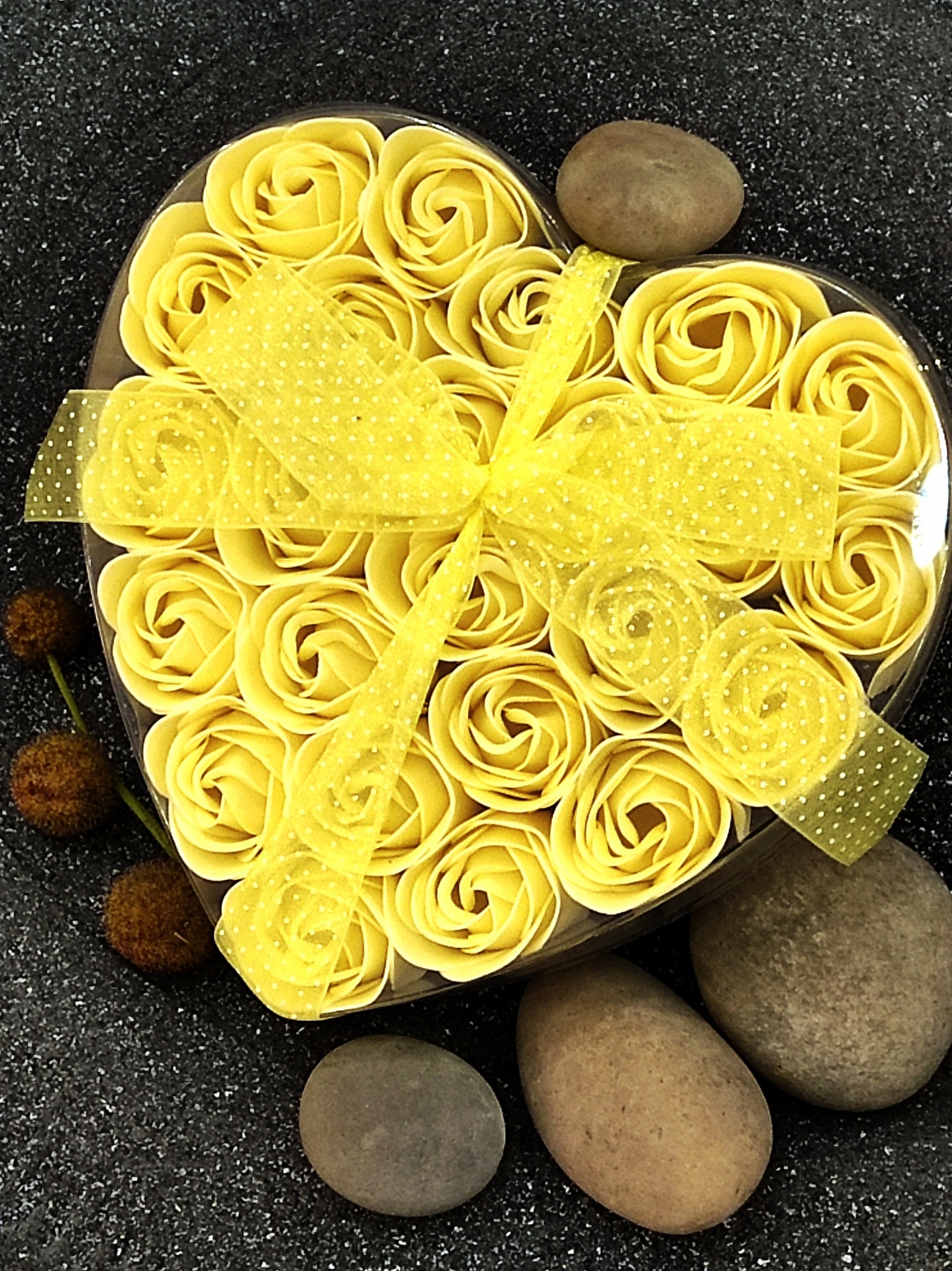 Caixa em forma de coração com flores amarelas decorativas e fita amarela, rodeada por pedras