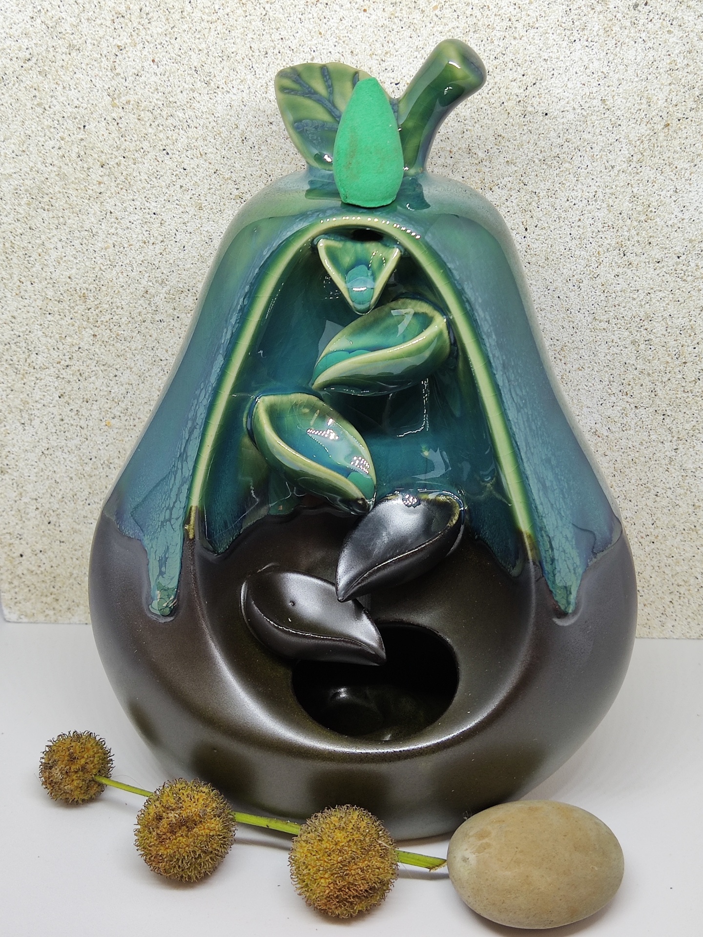 Fonte decorativa de cerâmica em forma de pêra verde e castanha com folhas interiores e elementos naturais ao lado