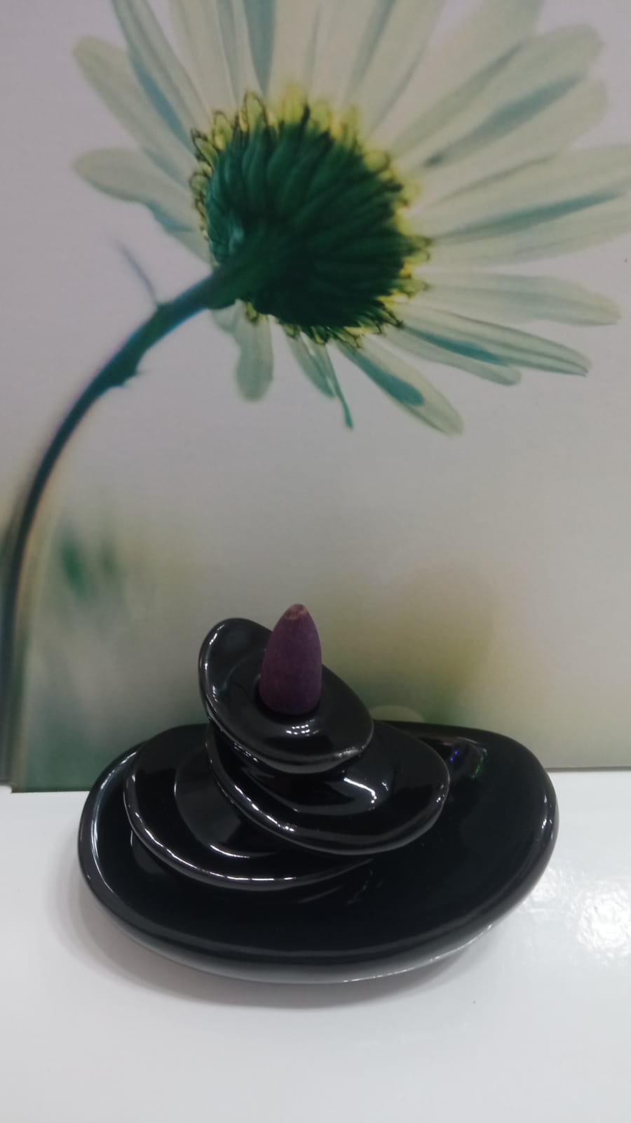 Incensário preto em cerâmica com cone de incenso roxo e flor branca ao fundo
