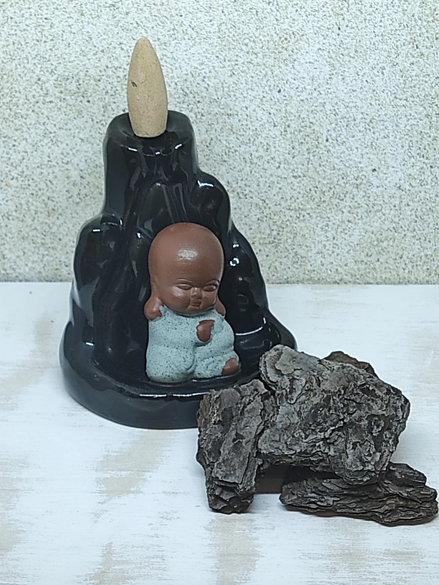 Incensário preto com estátua de bebé e cone de incenso ao lado de casca de árvore