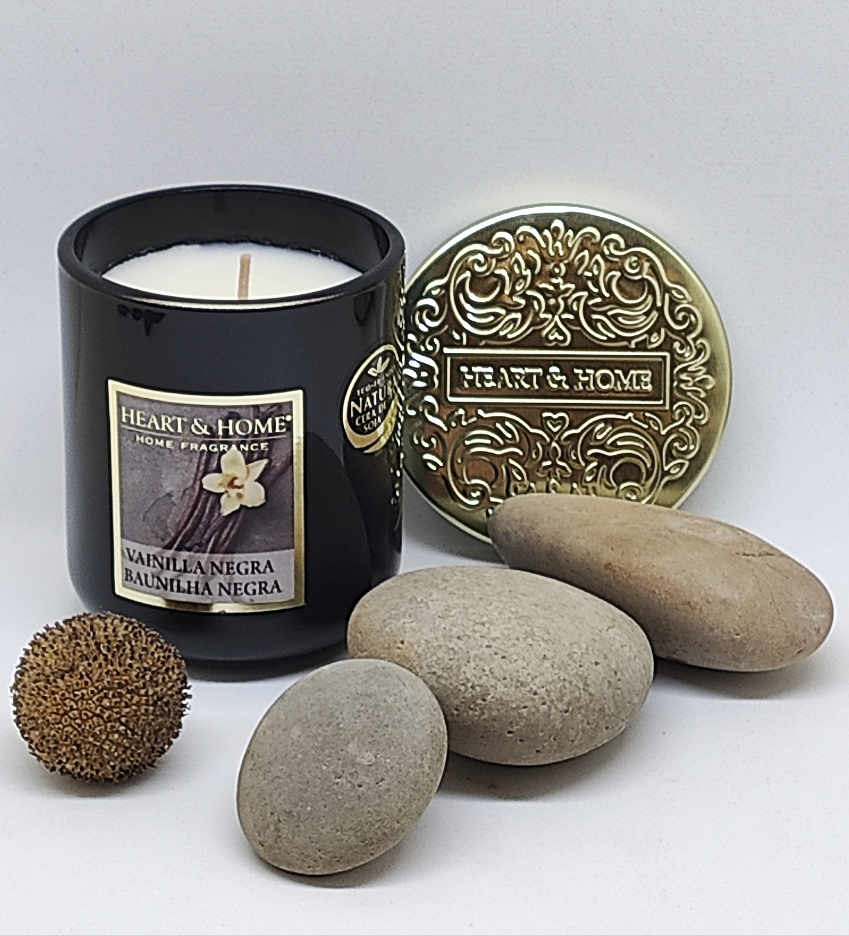 Vela perfumada com rótulo e tampa decorativa dourada, pedras naturais e semente marrom sobre fundo branco