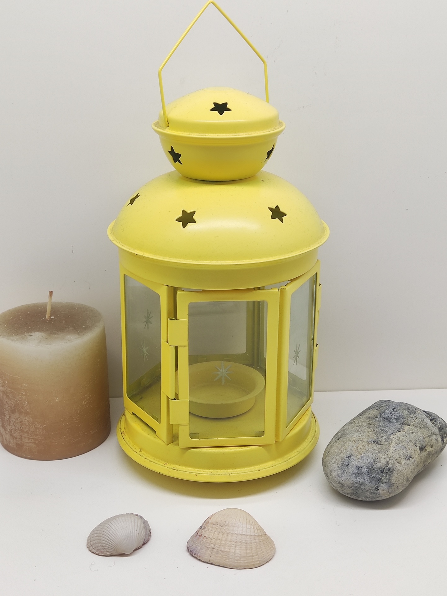 Lanterna metálica amarela com decoração de estrelas e vela castanha em fundo branco