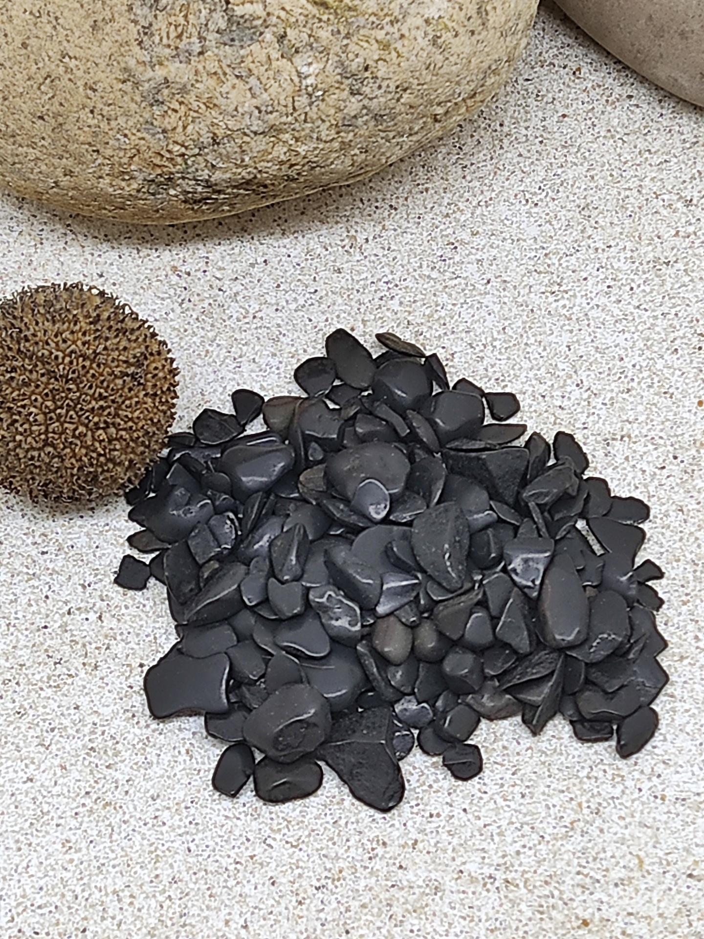 Pequenas pedras pretas em superfície clara com pedras grandes ao fundo