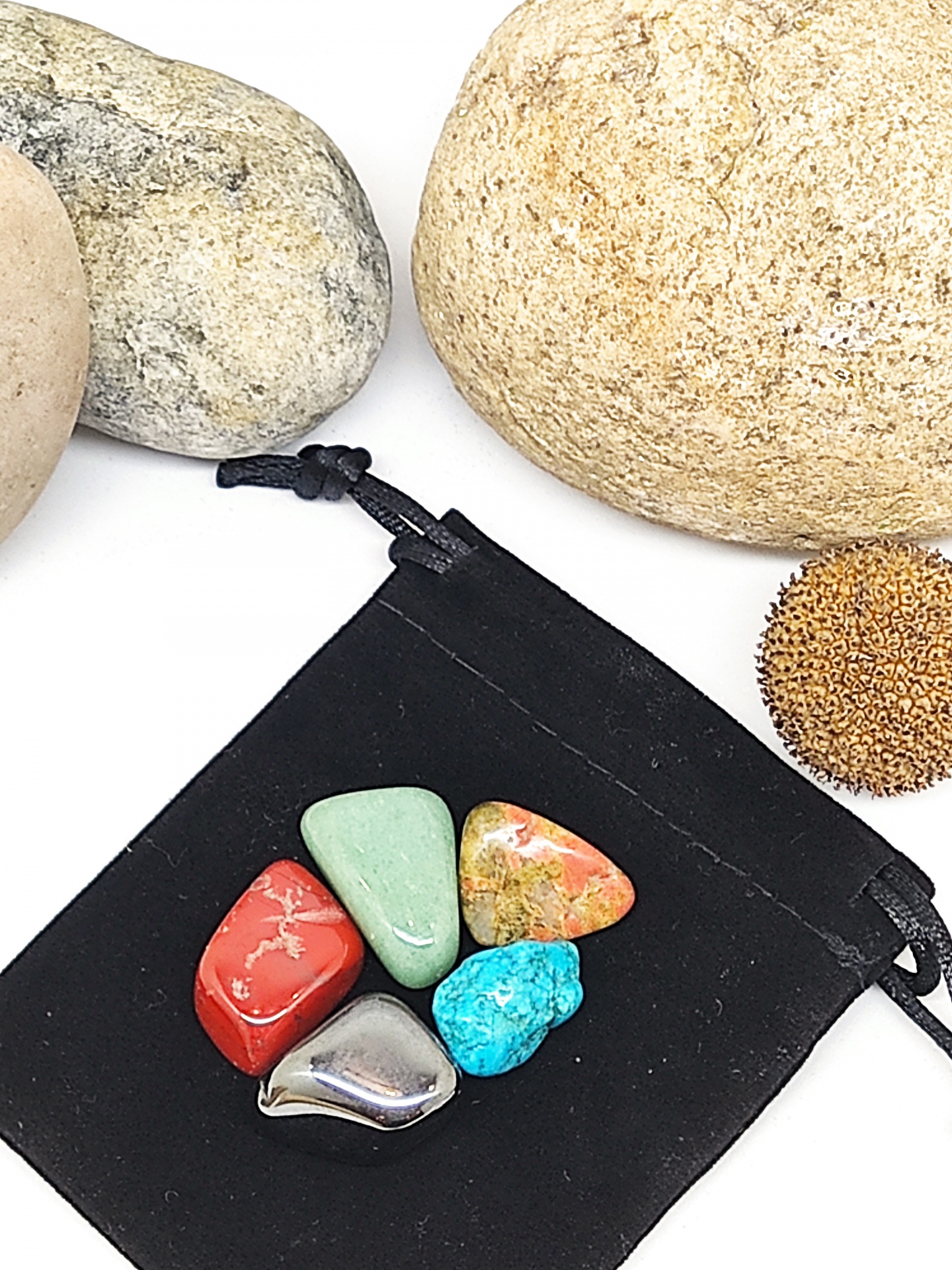 Pedras polidas coloridas sobre bolsa preta com pedras naturais ao fundo