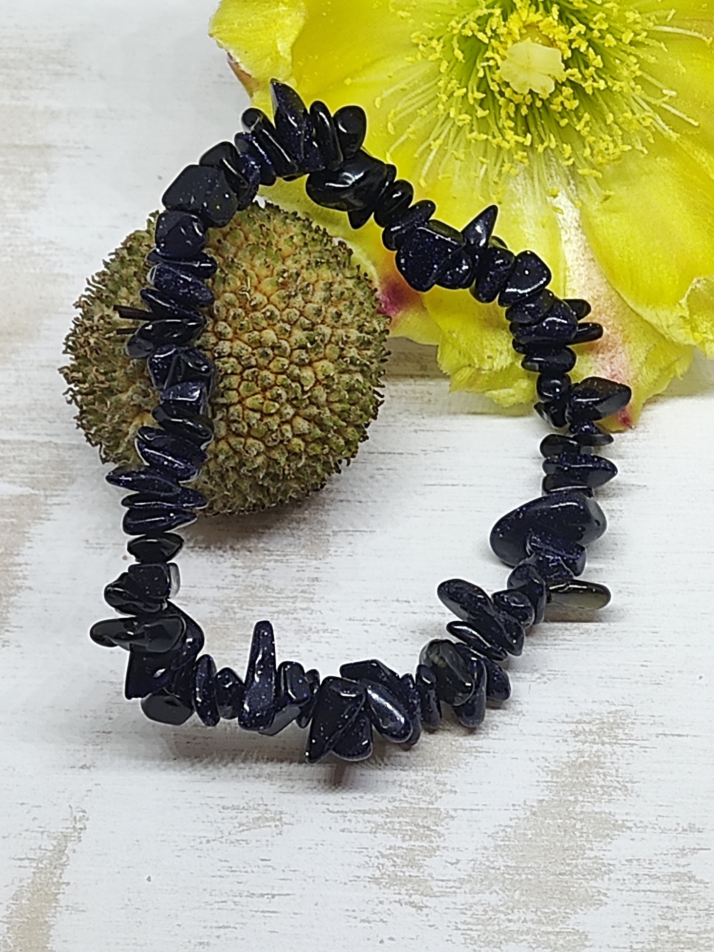 Pulseira de pedras pretas elástica com flor amarela e semente ao lado