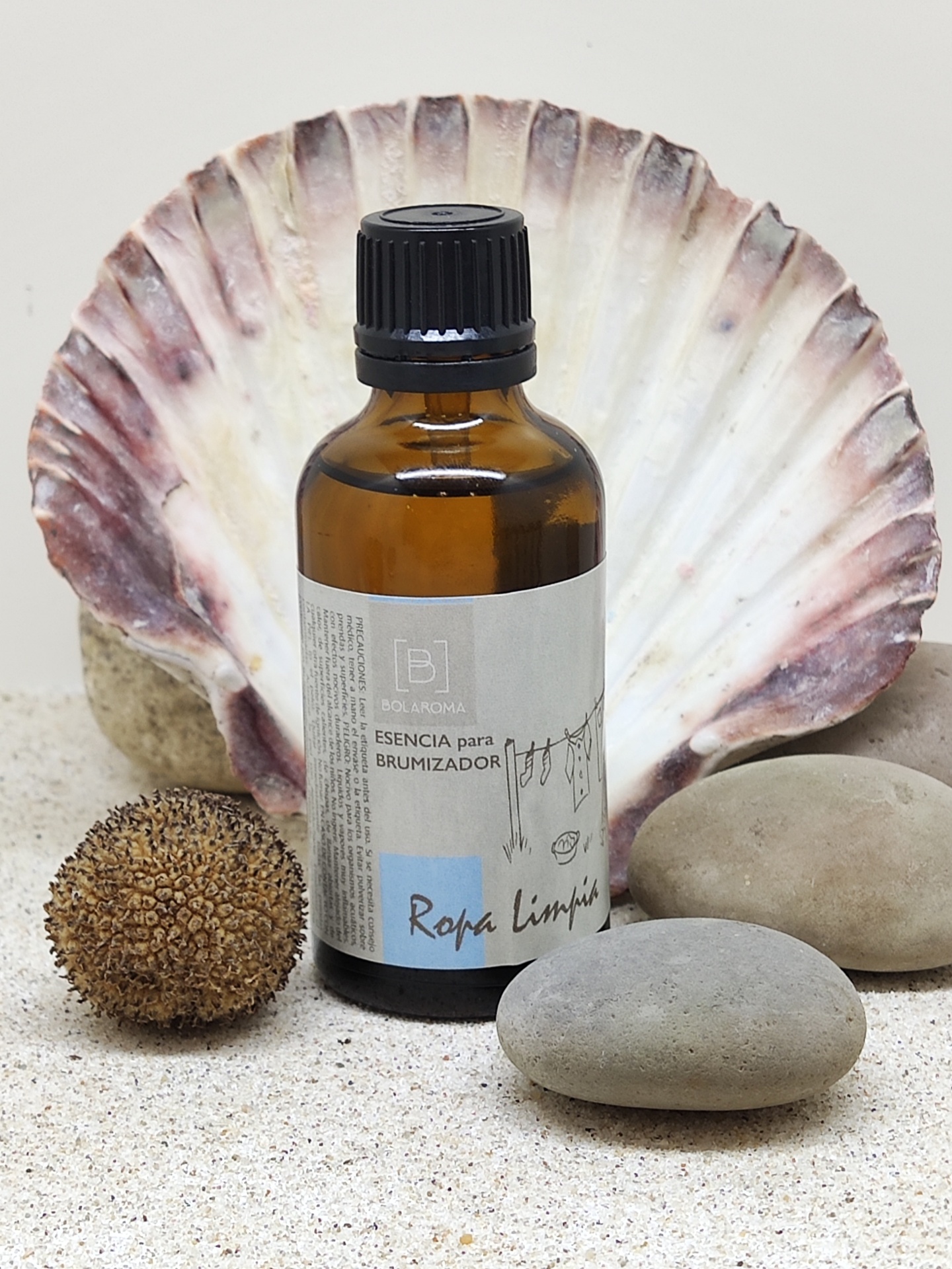 Frasco âmbar com essência para brumizador com etiqueta, concha e pedras sobre areia