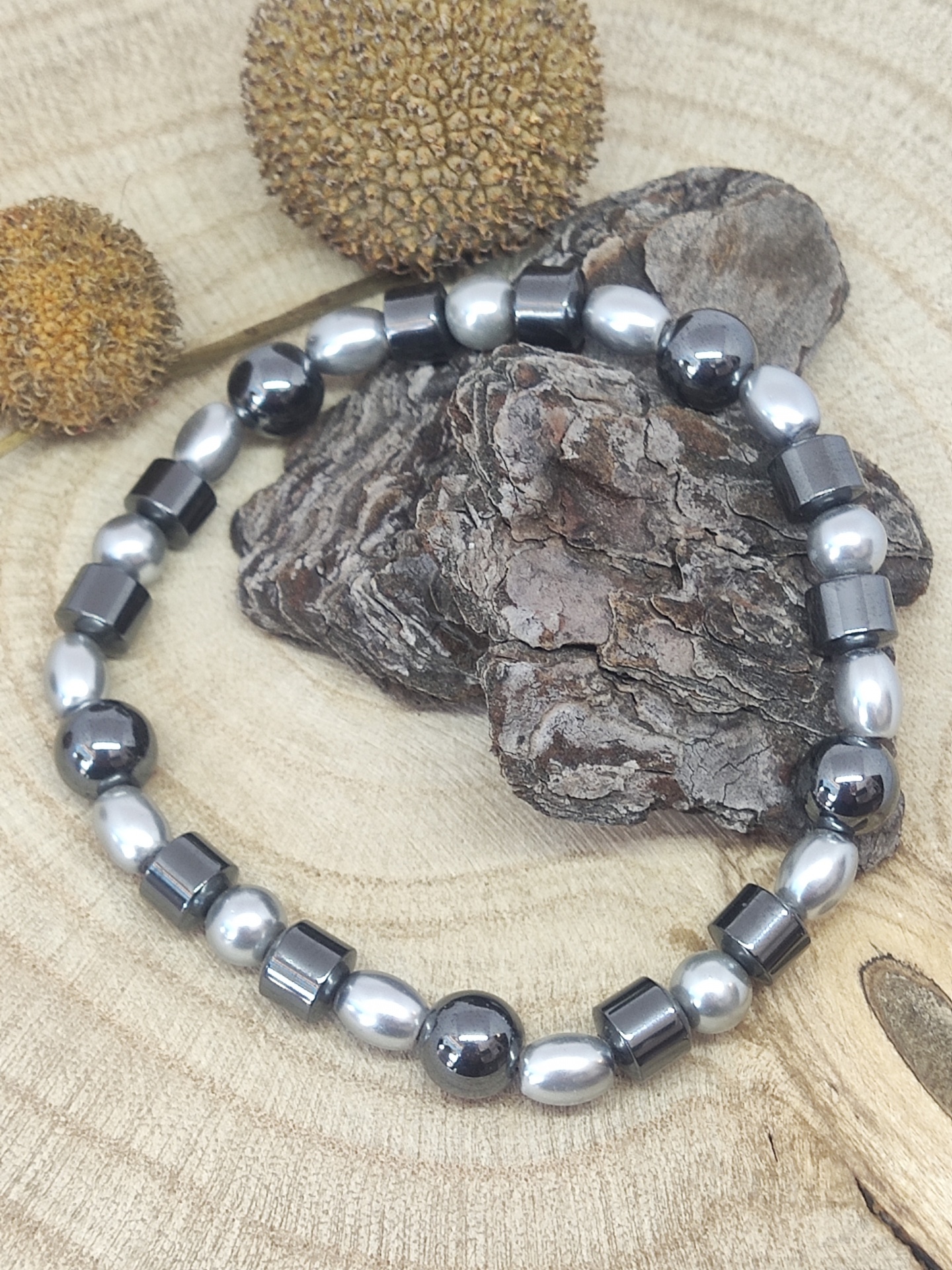 Pulseira metálica em diferentes formatos sobre casca de árvore e fundo de madeira